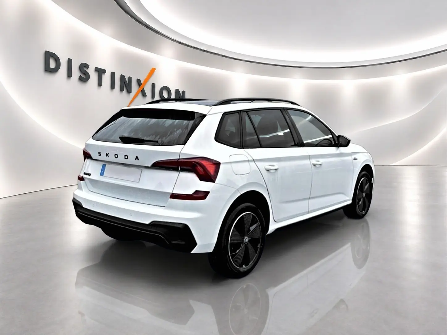 Vue 3/4 arrière droite d'un Skoda Kamiq blanc nacré avec jantes noires et toit noir dans un showroom lumineux.