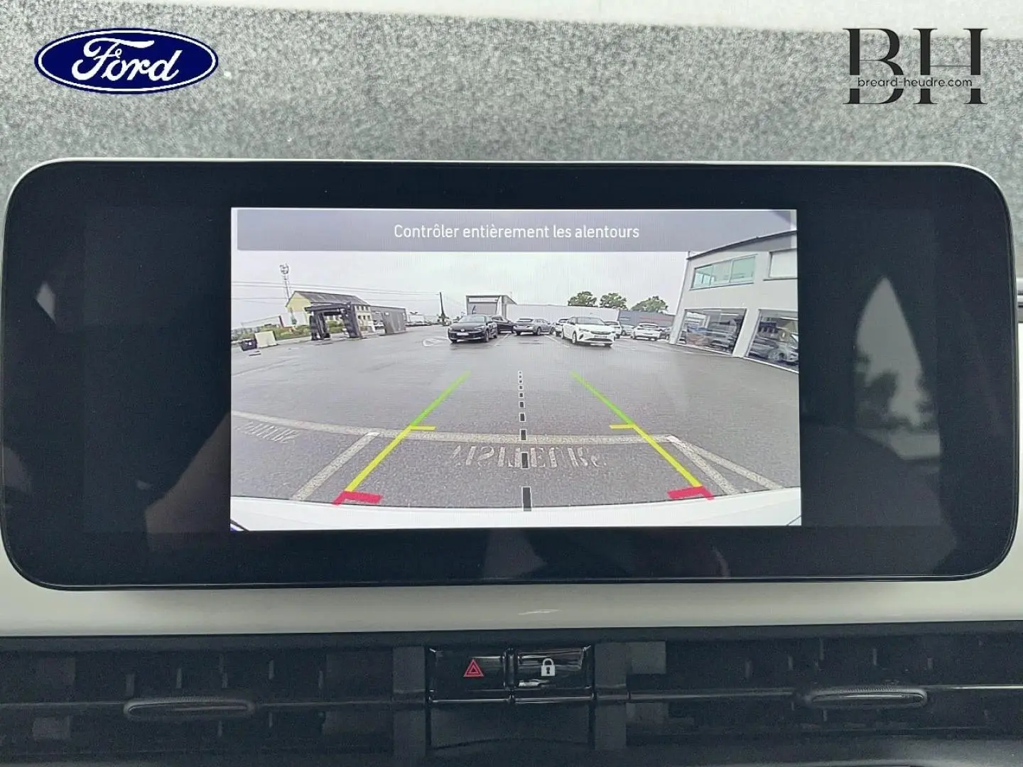 Écran de caméra de recul dans une Ford, affichant une vue arrière sur un parking avec plusieurs voitures visibles.