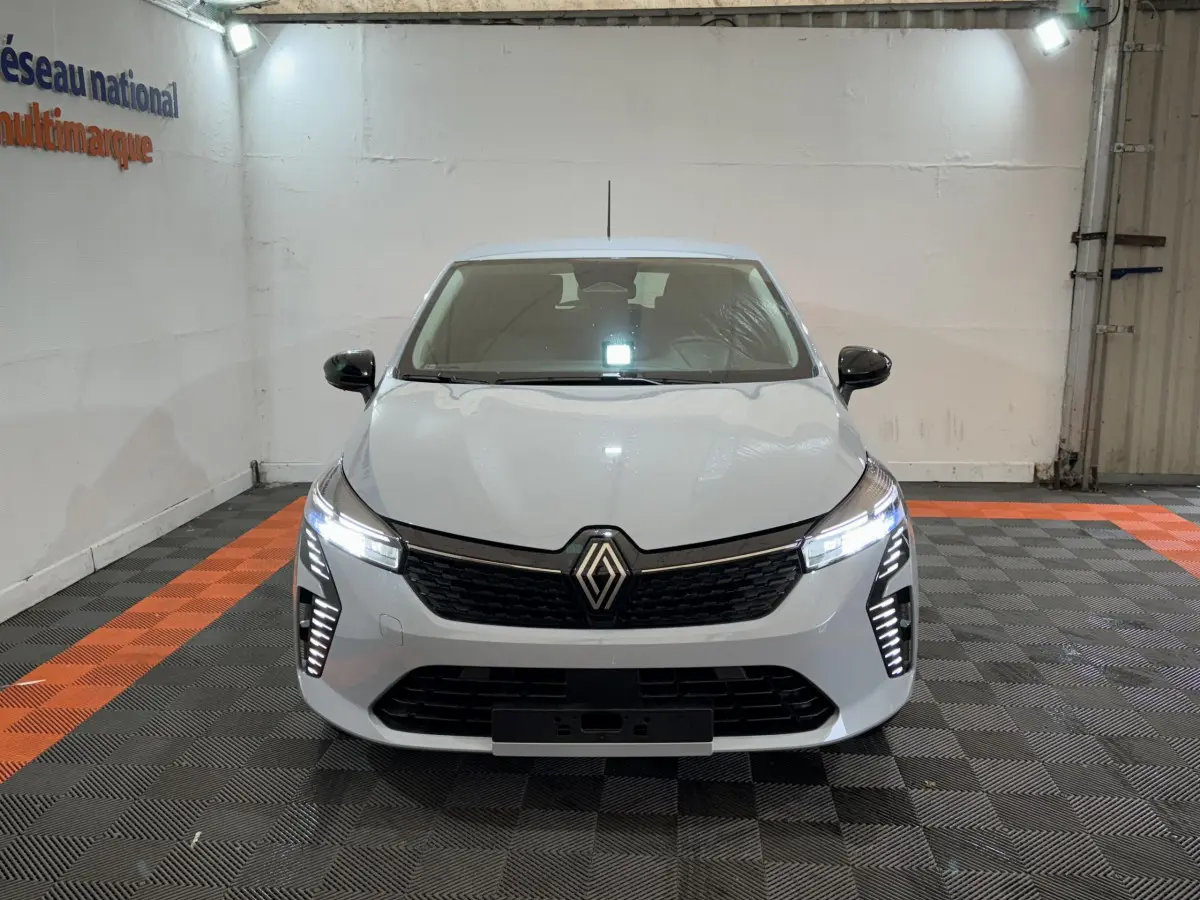 Renault Clio gris clair vue de face en intérieur, avec phares LED allumés et calandre noire distinctive.