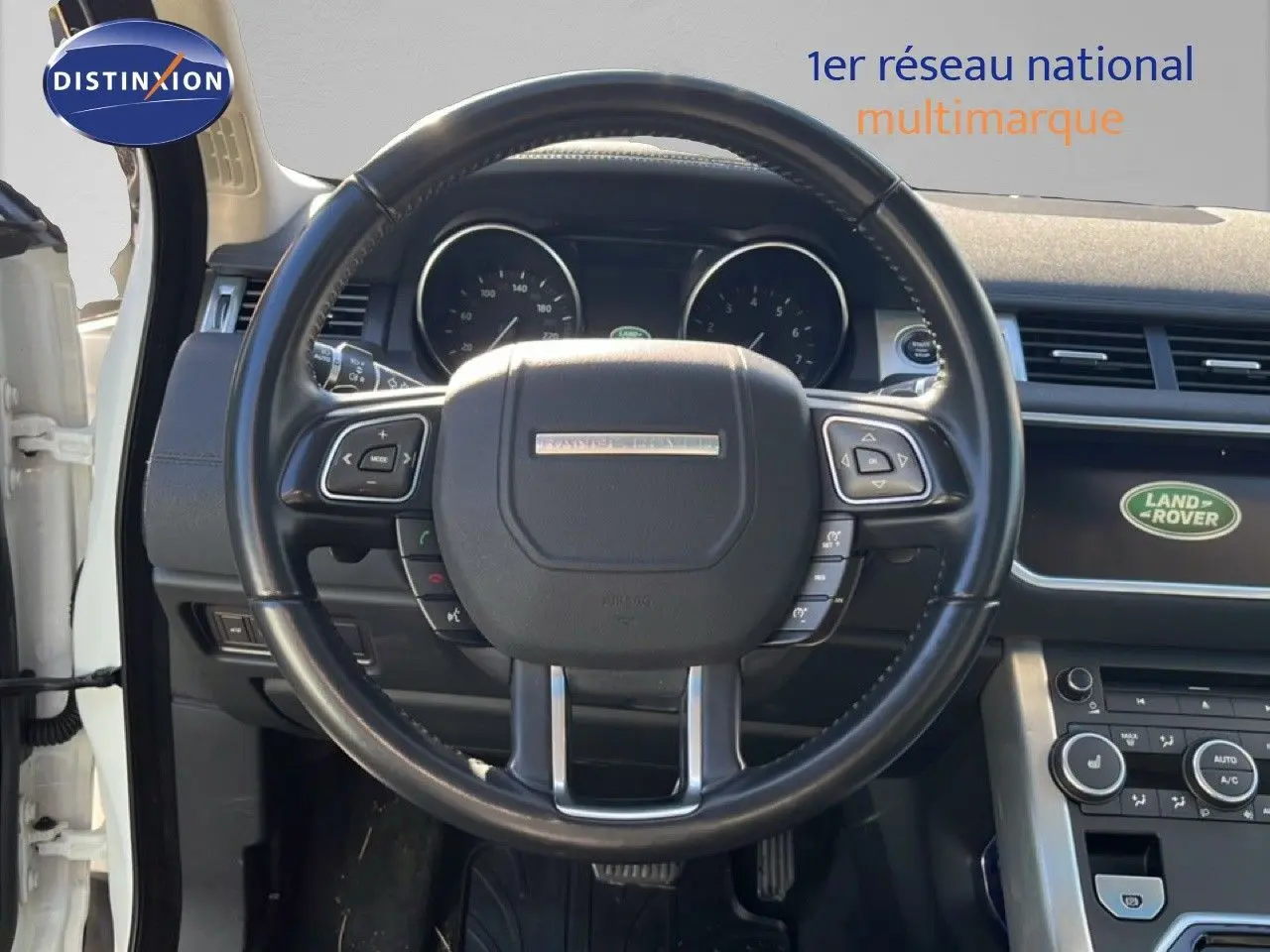 Vue intérieure centrée sur le volant noir du Range Rover Evoque blanc de 2017 avec tableau de bord et écran Land Rover visible.