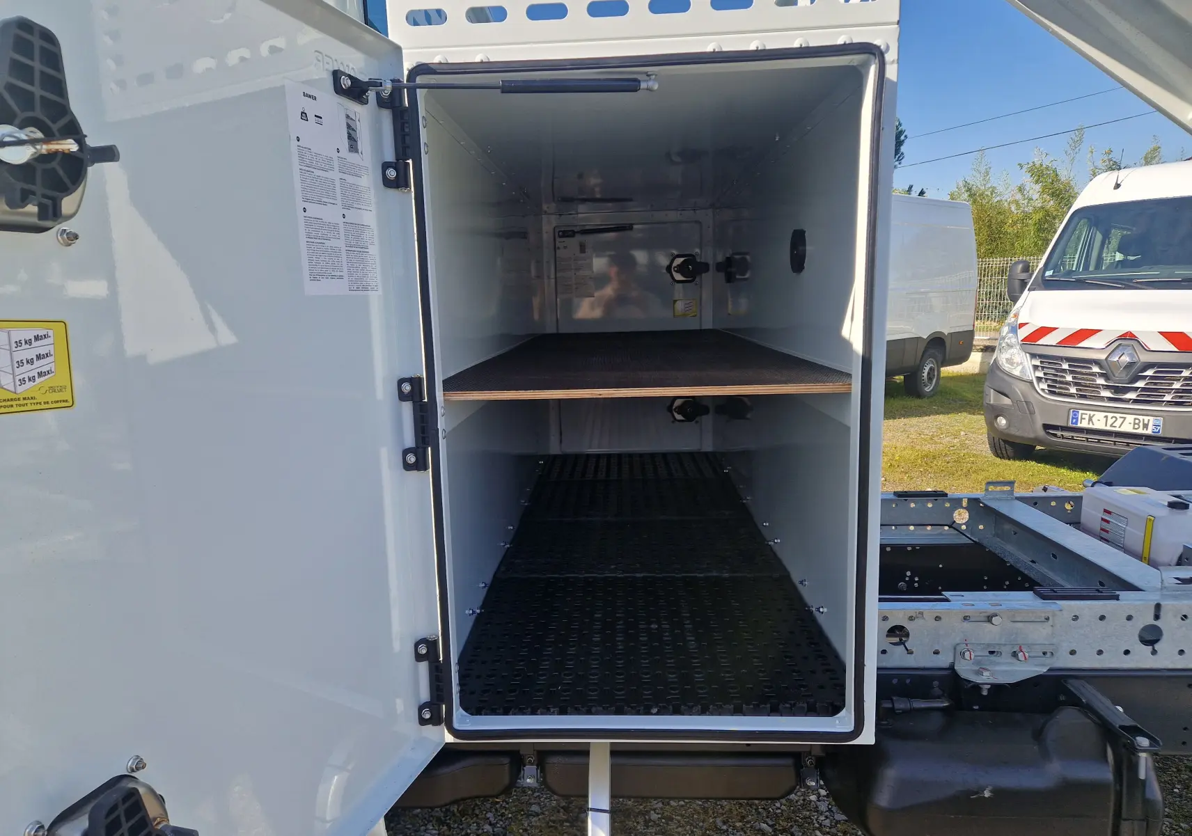 Vue de face du coffre blanc ouvert du châssis cabine Iveco Daily 35C16 avec benne acier et étagère intérieure visible.