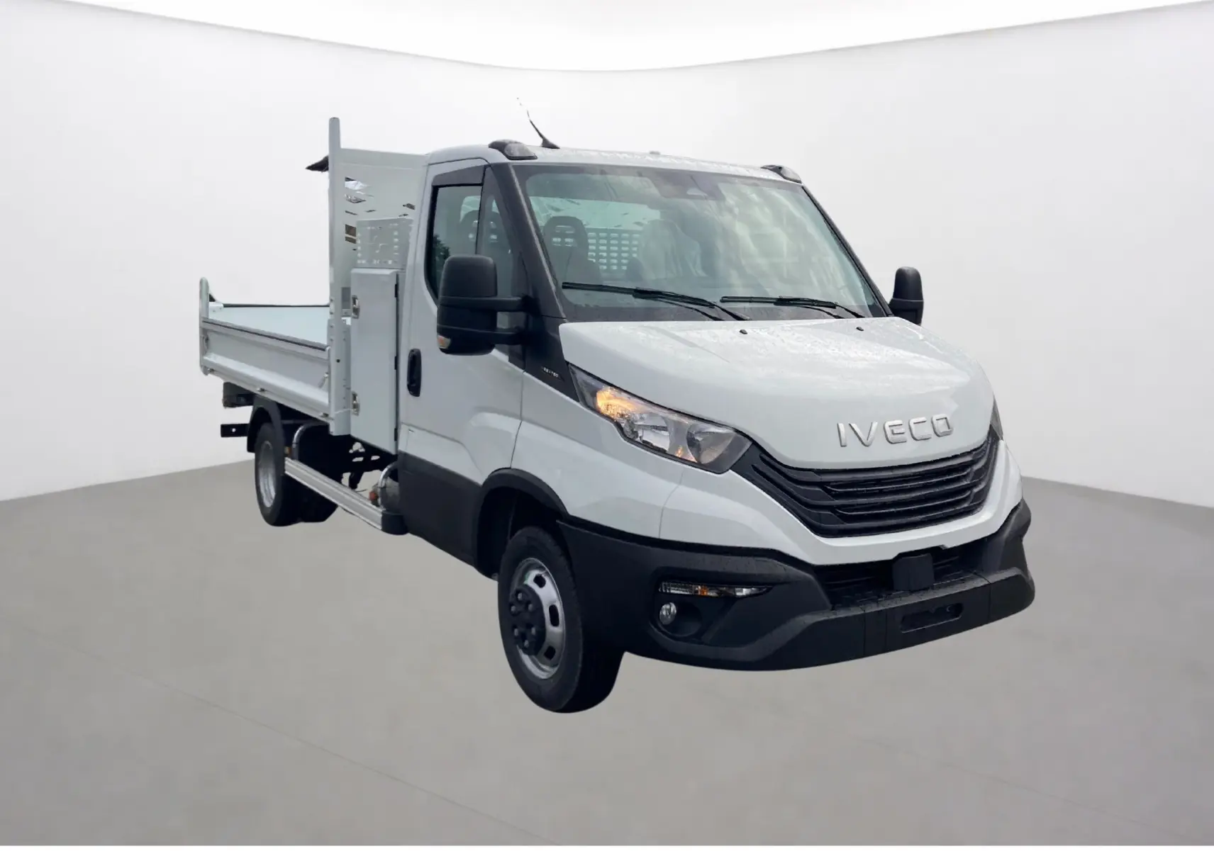 Vue 3/4 avant droit d’un utilitaire blanc Iveco Daily Châssis cabine avec benne acier et coffre latéral.