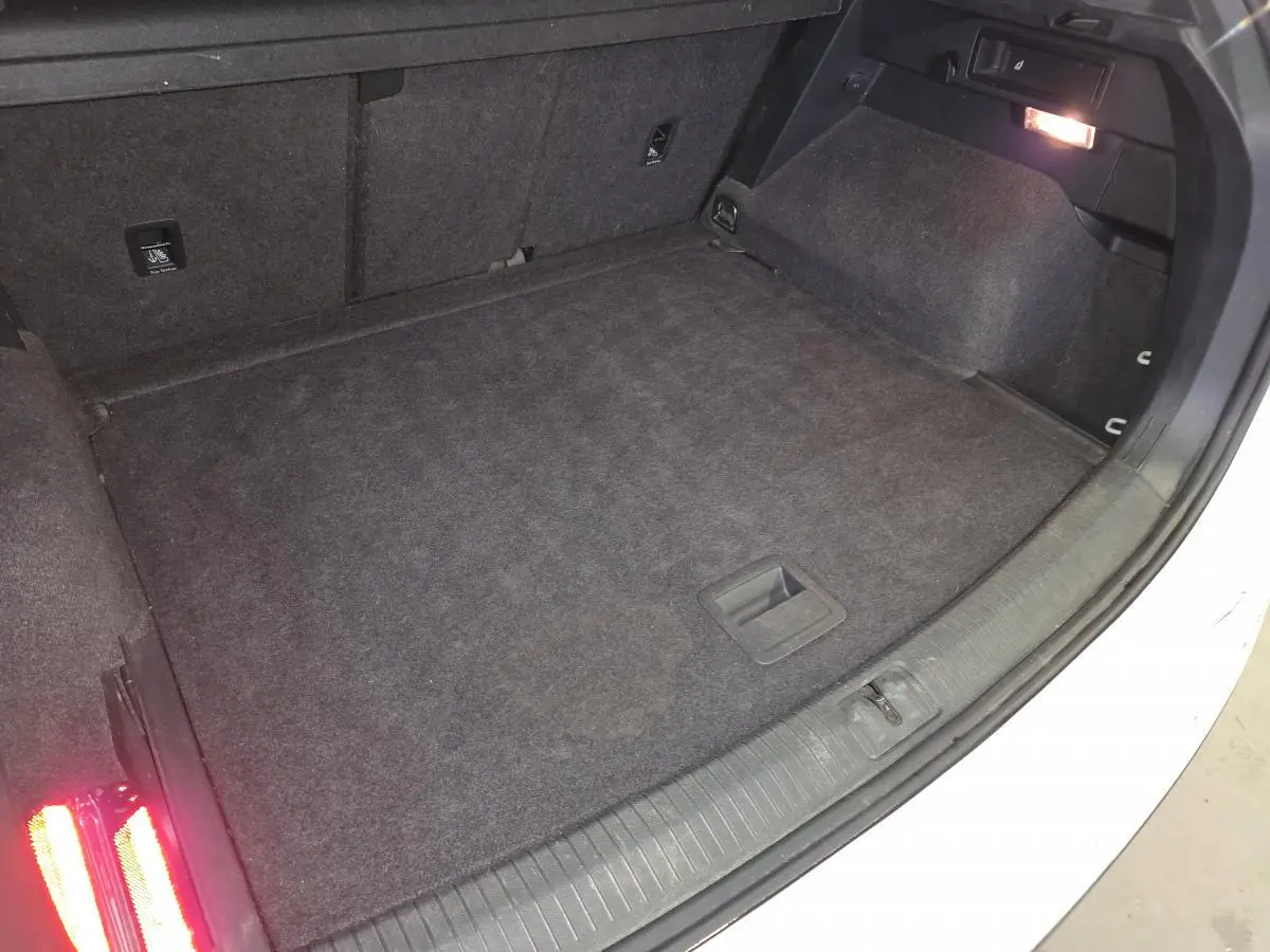 Coffre ouvert du Volkswagen Tiguan blanc, montrant le plancher modulable et l'éclairage intérieur à droite.