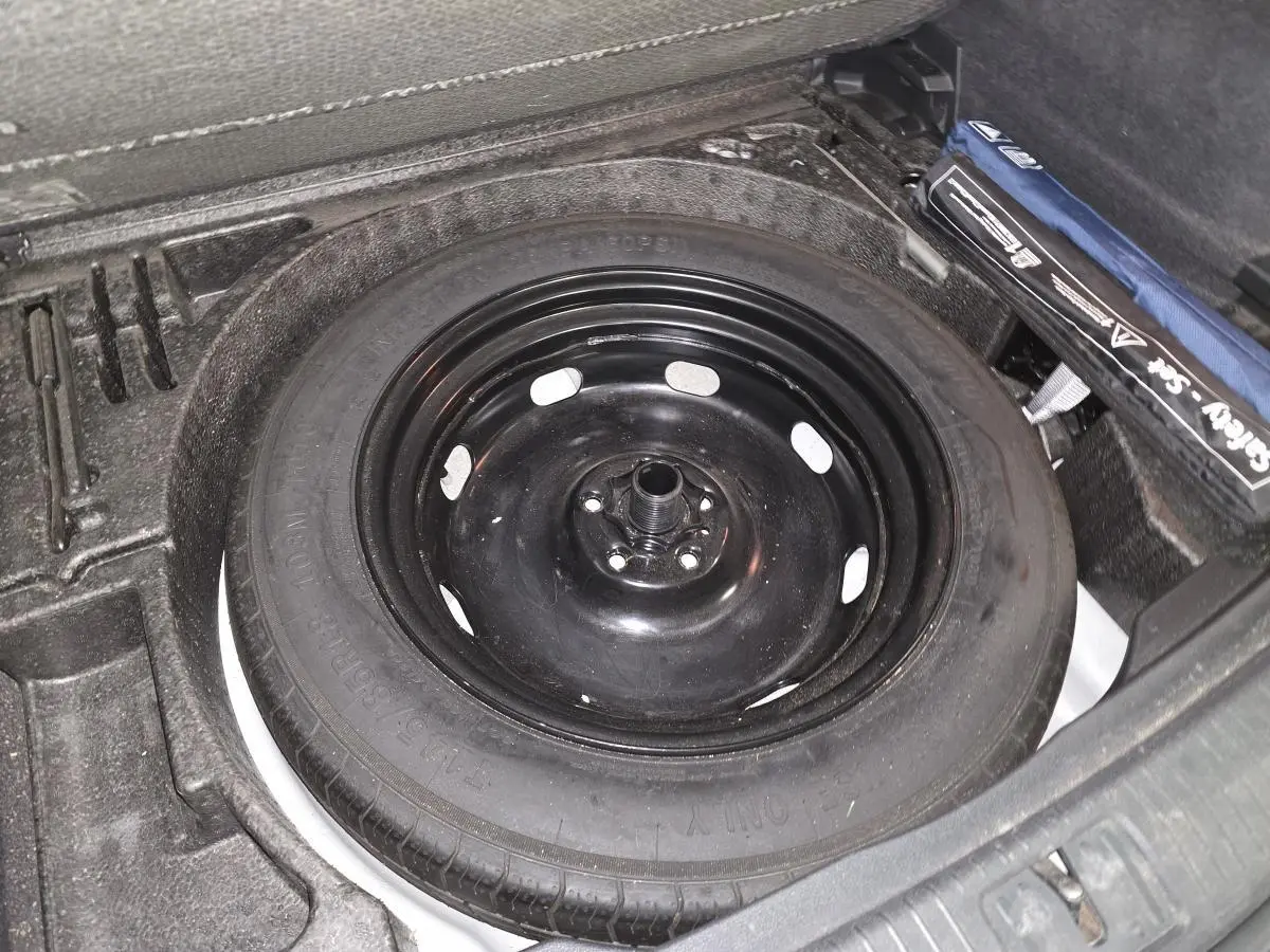 Gros plan sur la roue de secours noire dans le coffre modulable du Volkswagen Tiguan blanc.