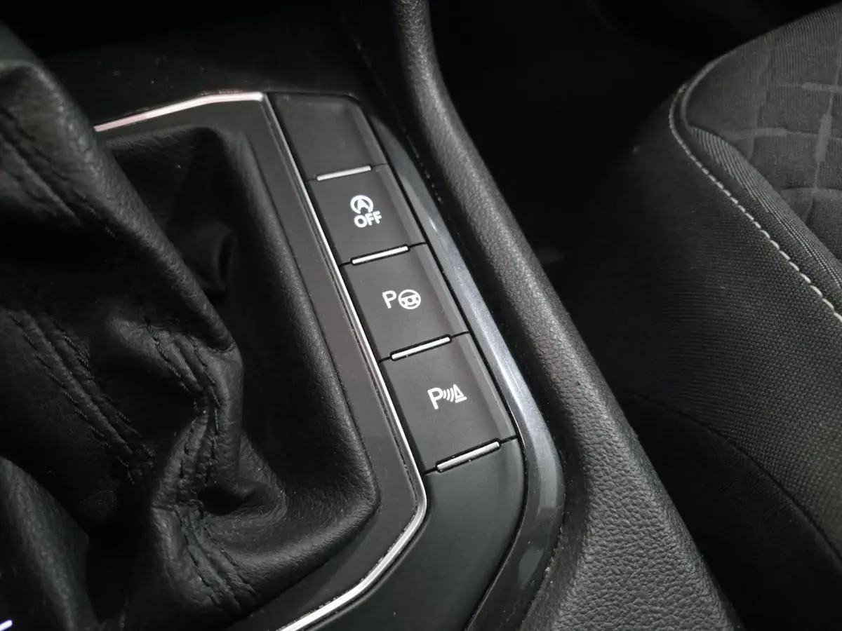 Gros plan sur la console centrale noire avec boutons de contrôle et partie de la sellerie tissu du Volkswagen Tiguan blanc.