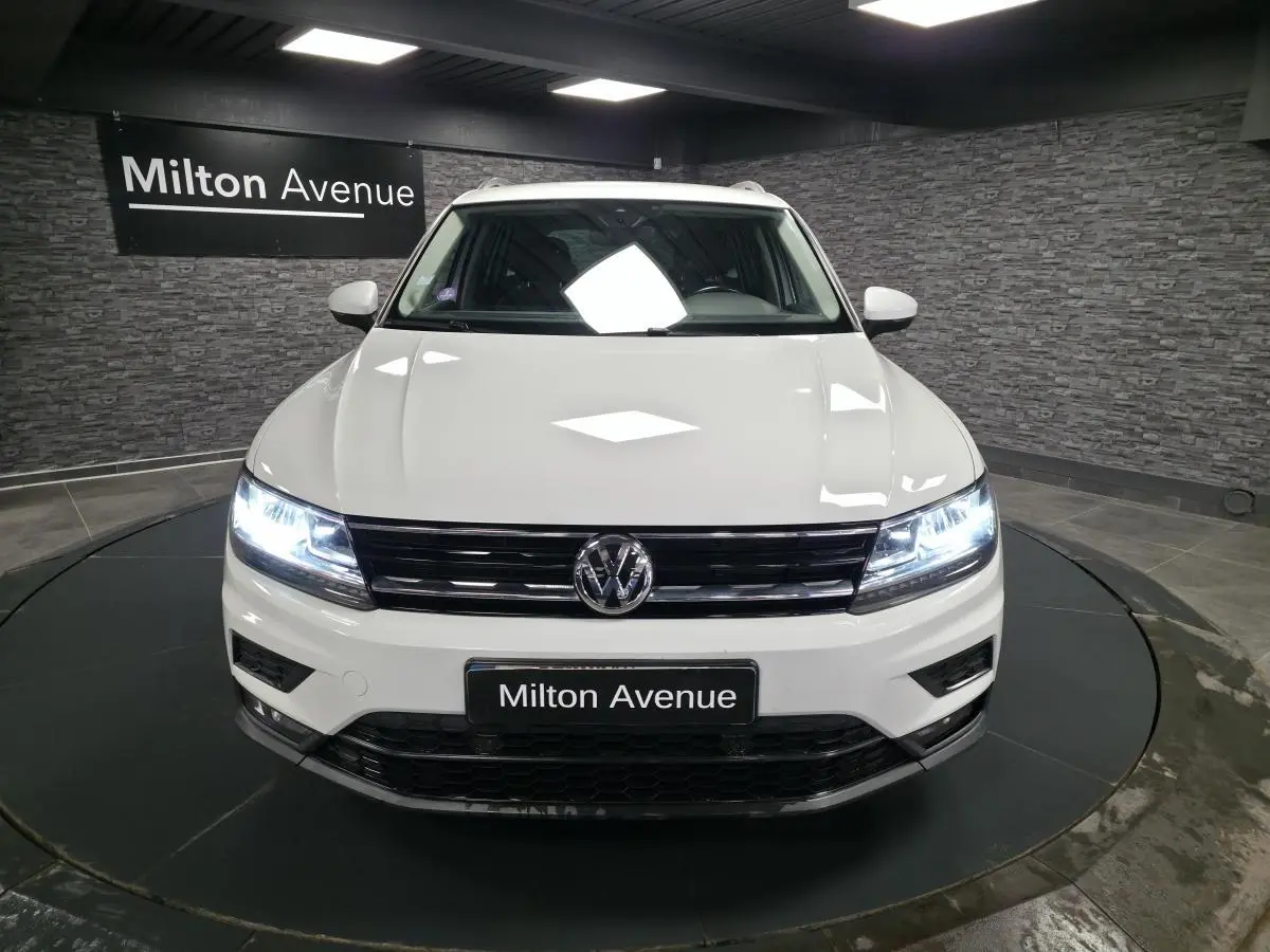 Vue de face du Volkswagen Tiguan blanc avec phares LED allumés dans un showroom au mur en pierre grise.