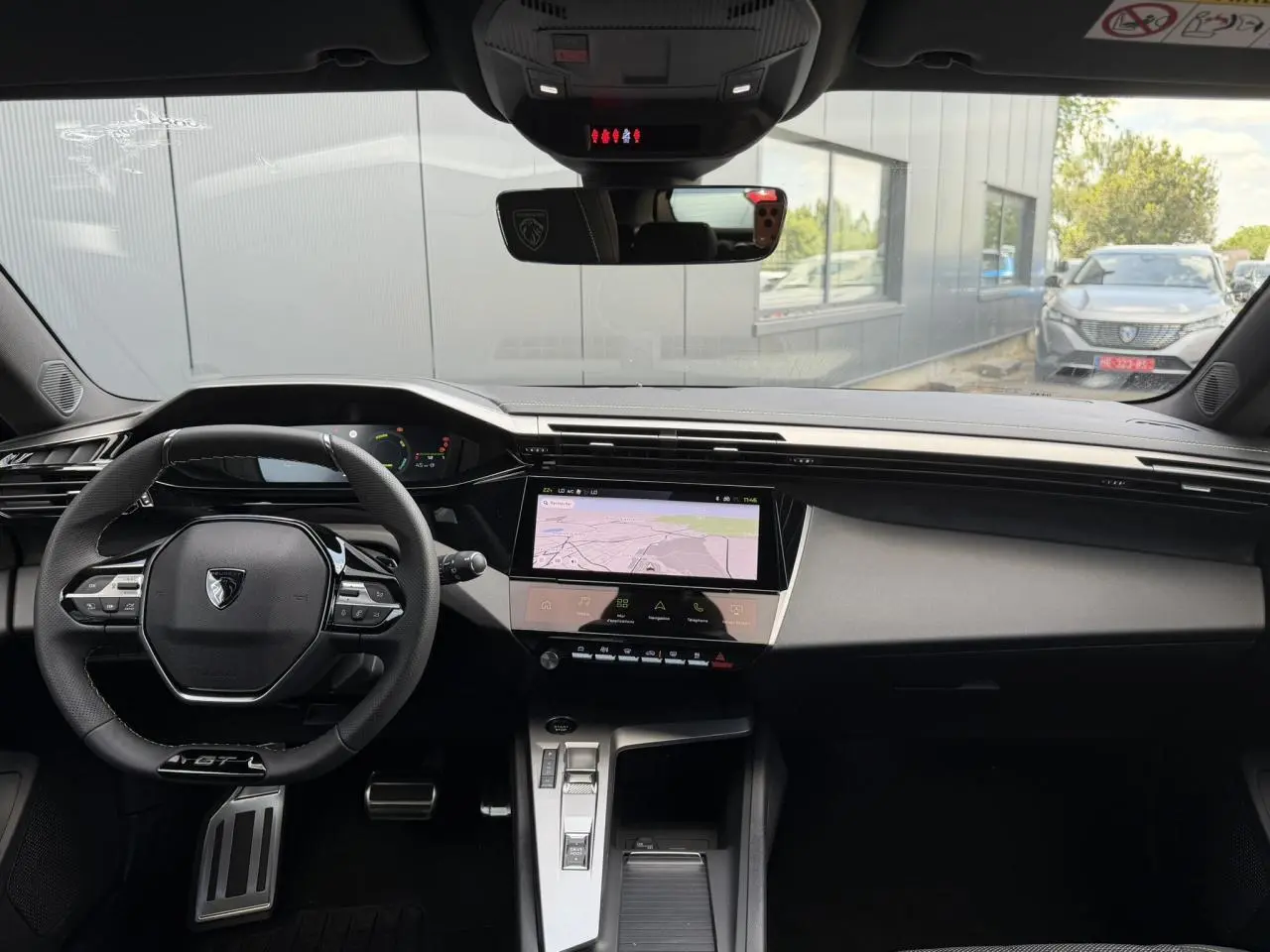 Vue intérieure avant du Peugeot 308 NV Hybrid 145 GT e-DSC6 2026, tableau de bord noir avec écran tactile central et volant GT cuir.