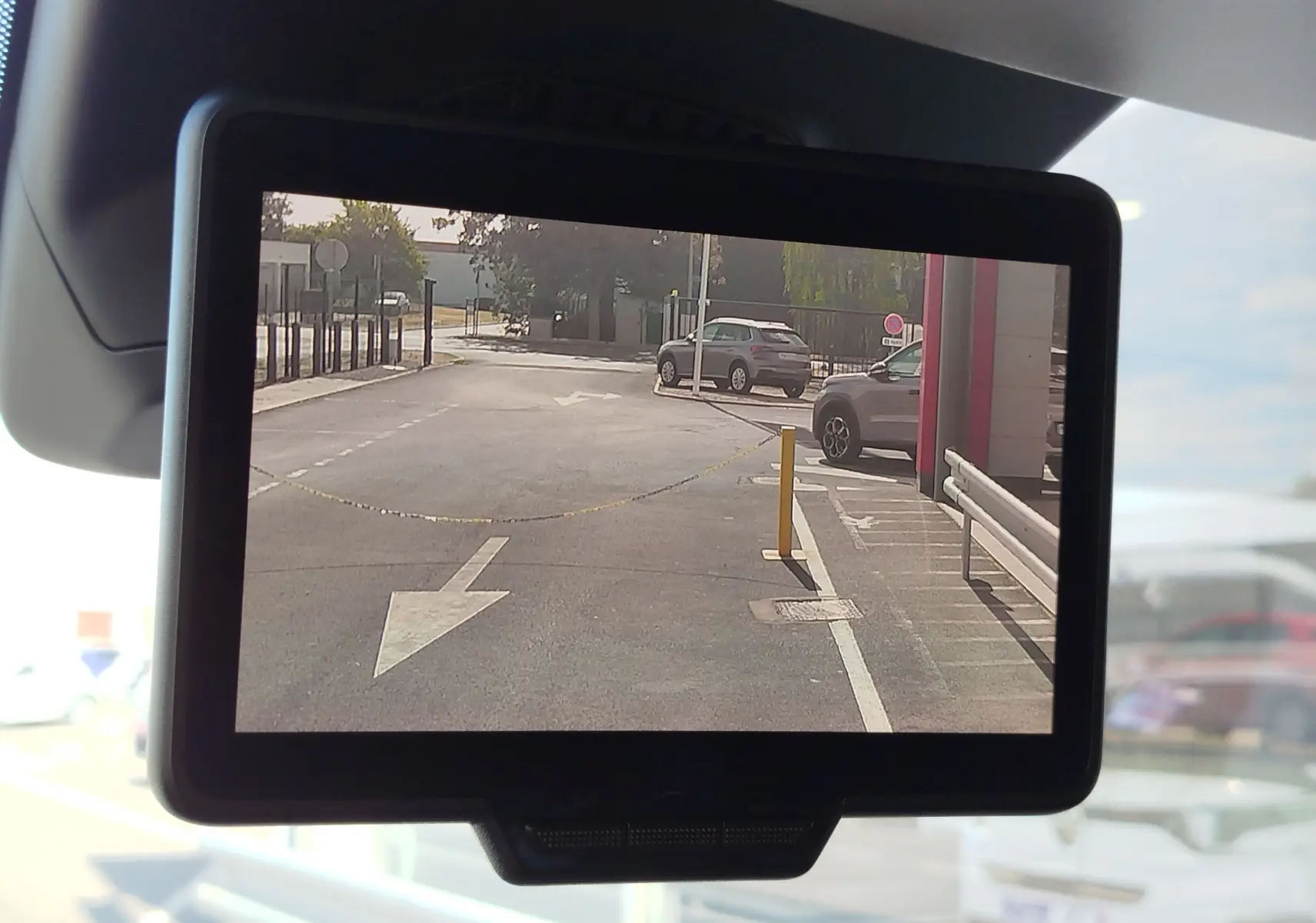 Vue de la caméra de recul du Renault Kangoo blanc, affichant une zone de stationnement avec flèche au sol et barrières.
