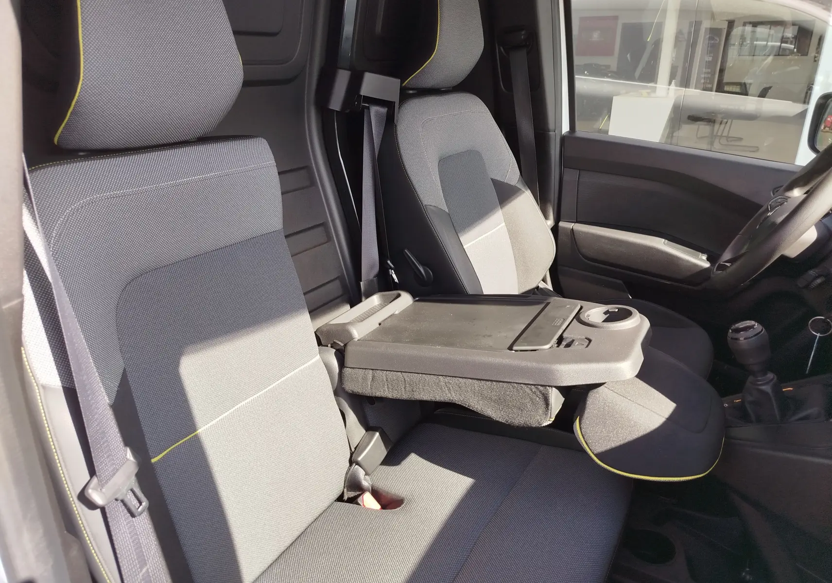Intérieur avant droit du Renault Kangoo 2023 blanc, sièges gris avec surpiqûres jaunes et tablette rabattable centrale.
