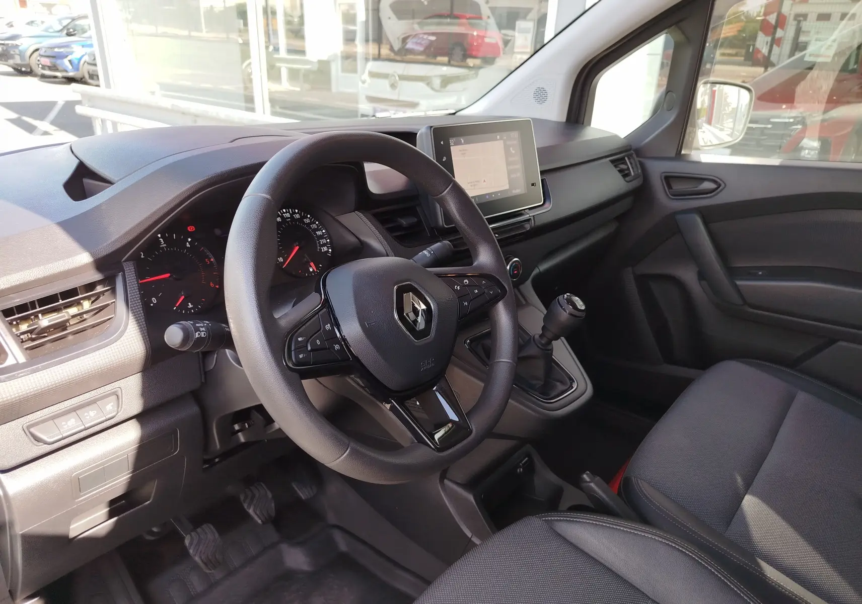 Vue intérieure côté conducteur du Renault Kangoo 2023, volant multifonction et écran tactile central visible.