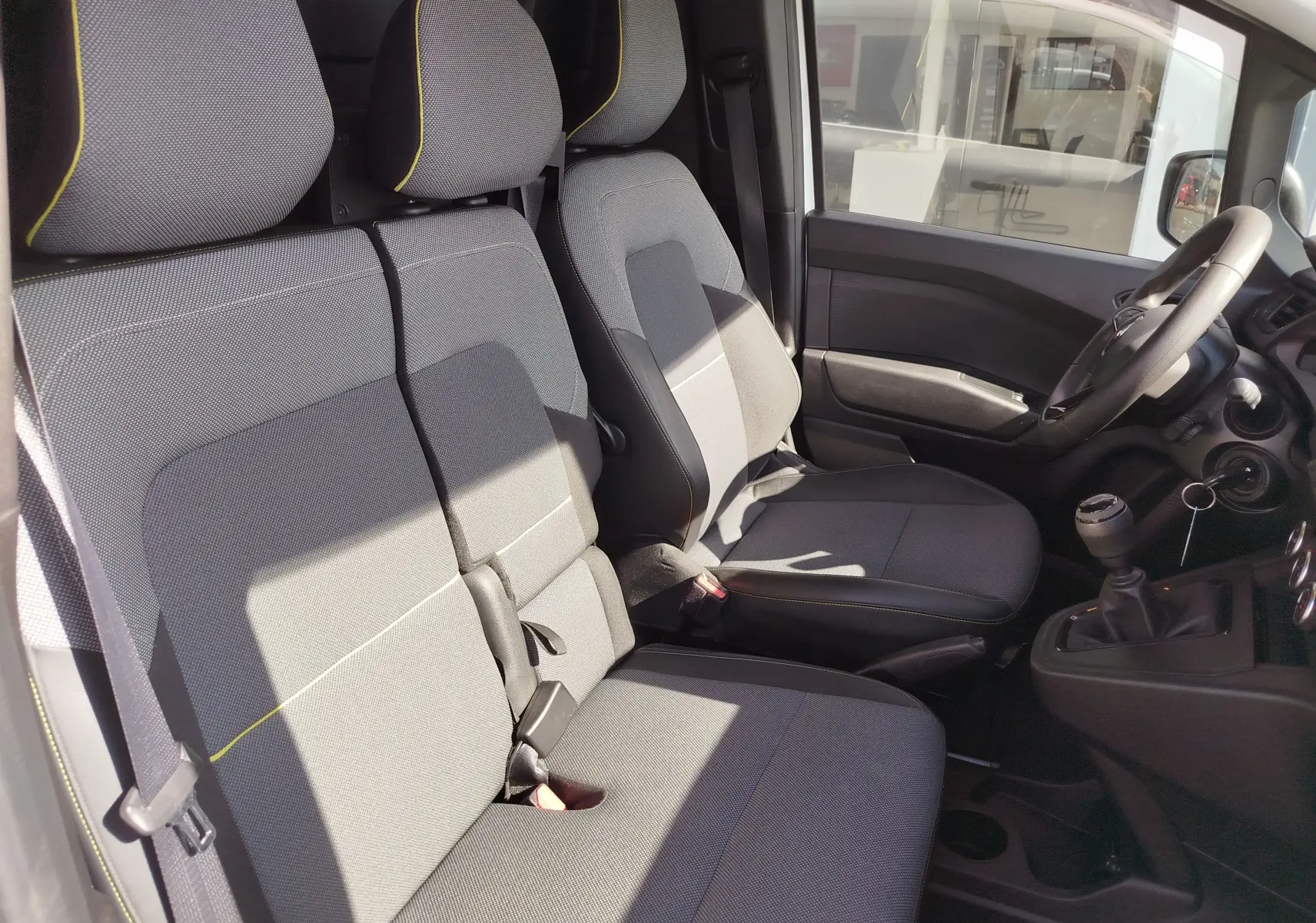 Vue intérieure côté conducteur du Renault Kangoo 2023, sièges gris avec surpiqûres jaunes et volant multifonction.