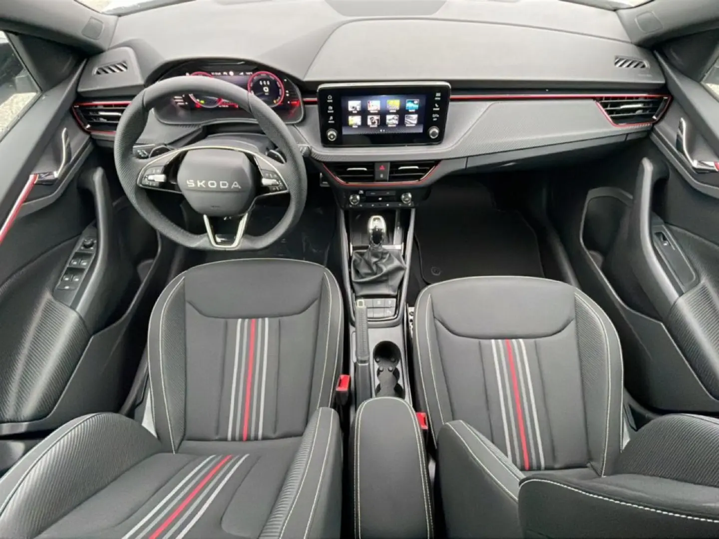 Vue intérieure avant du Skoda Kamiq 2026 avec sièges sport noirs à bandes rouges et tableau de bord moderne.