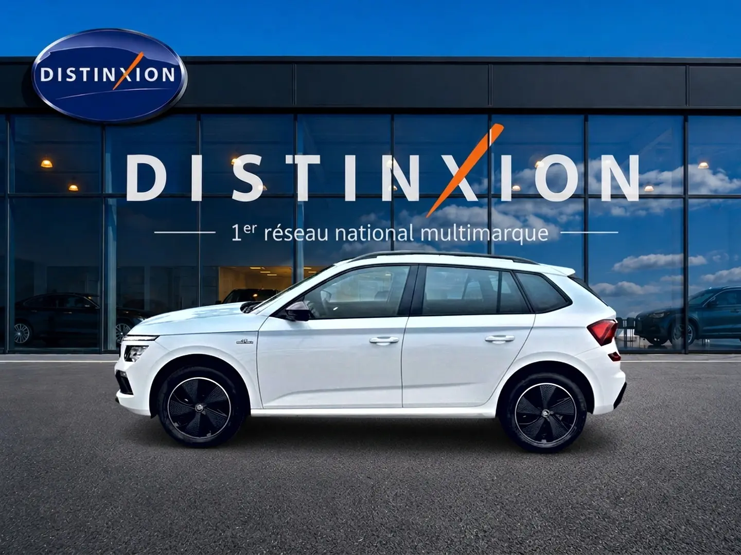 Profil droit d’un Skoda Kamiq blanc nacré 2026 avec jantes noires et toit blanc devant un showroom Distinxion.