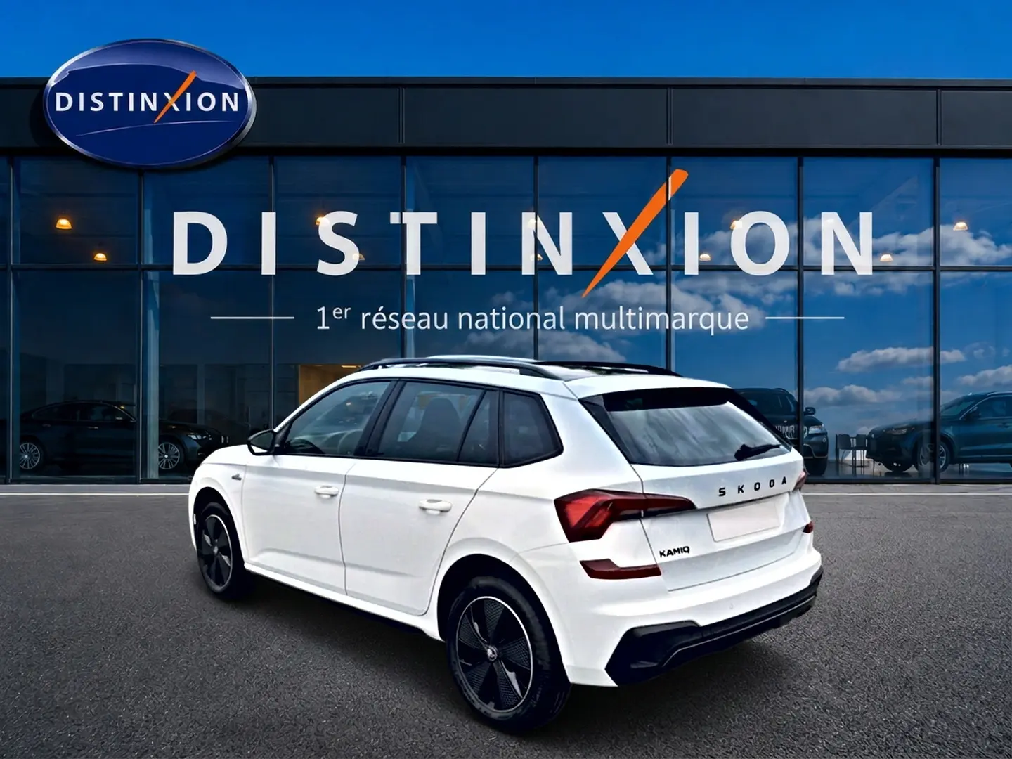 Vue 3/4 arrière droite d'un Skoda Kamiq blanc nacré avec jantes noires et toit panoramique, devant une vitrine Distinxion.