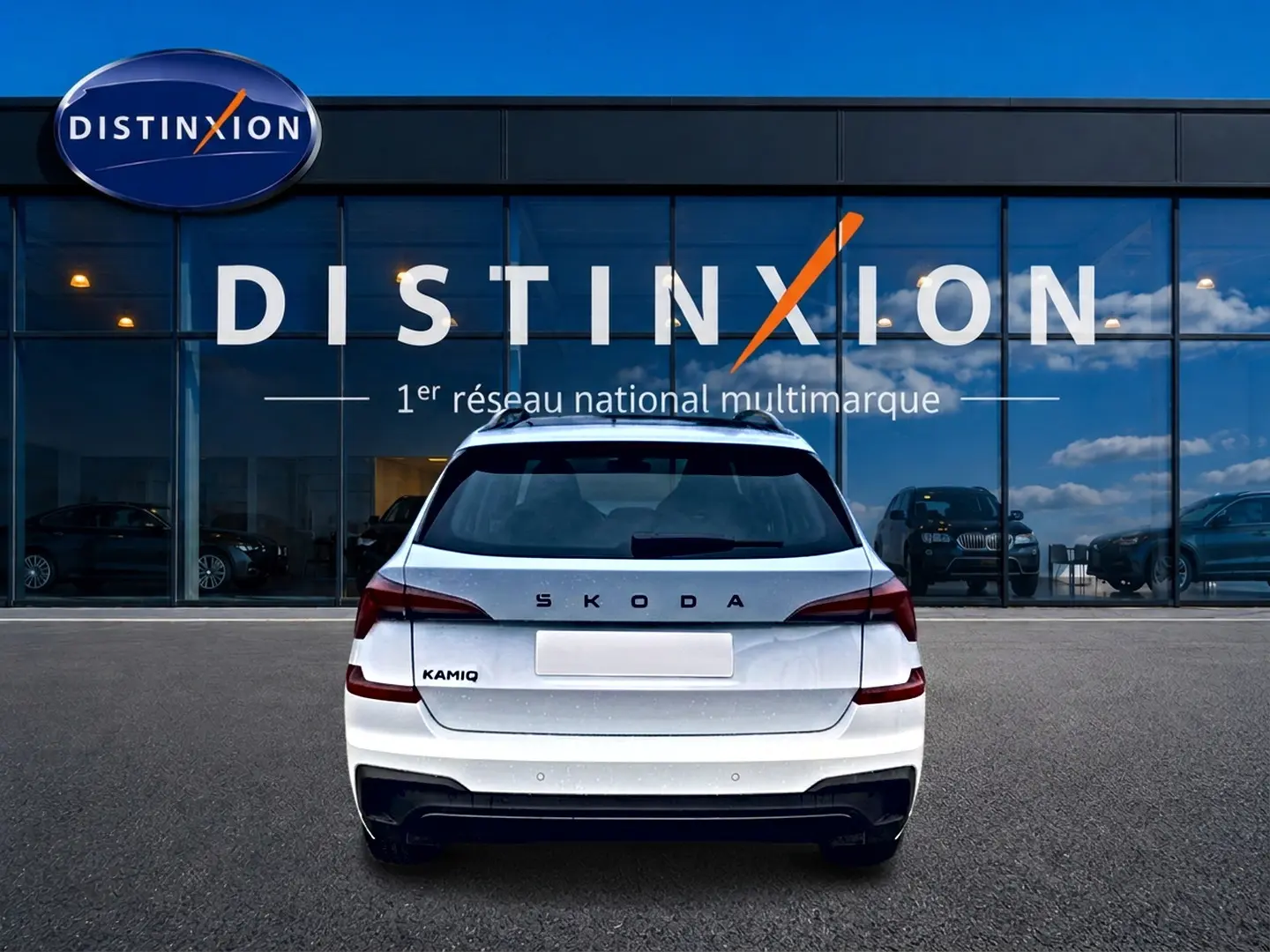 Vue arrière d'un Skoda Kamiq blanc nacré avec logo distinctif et diffuseur noir, devant une vitrine Distinxion.