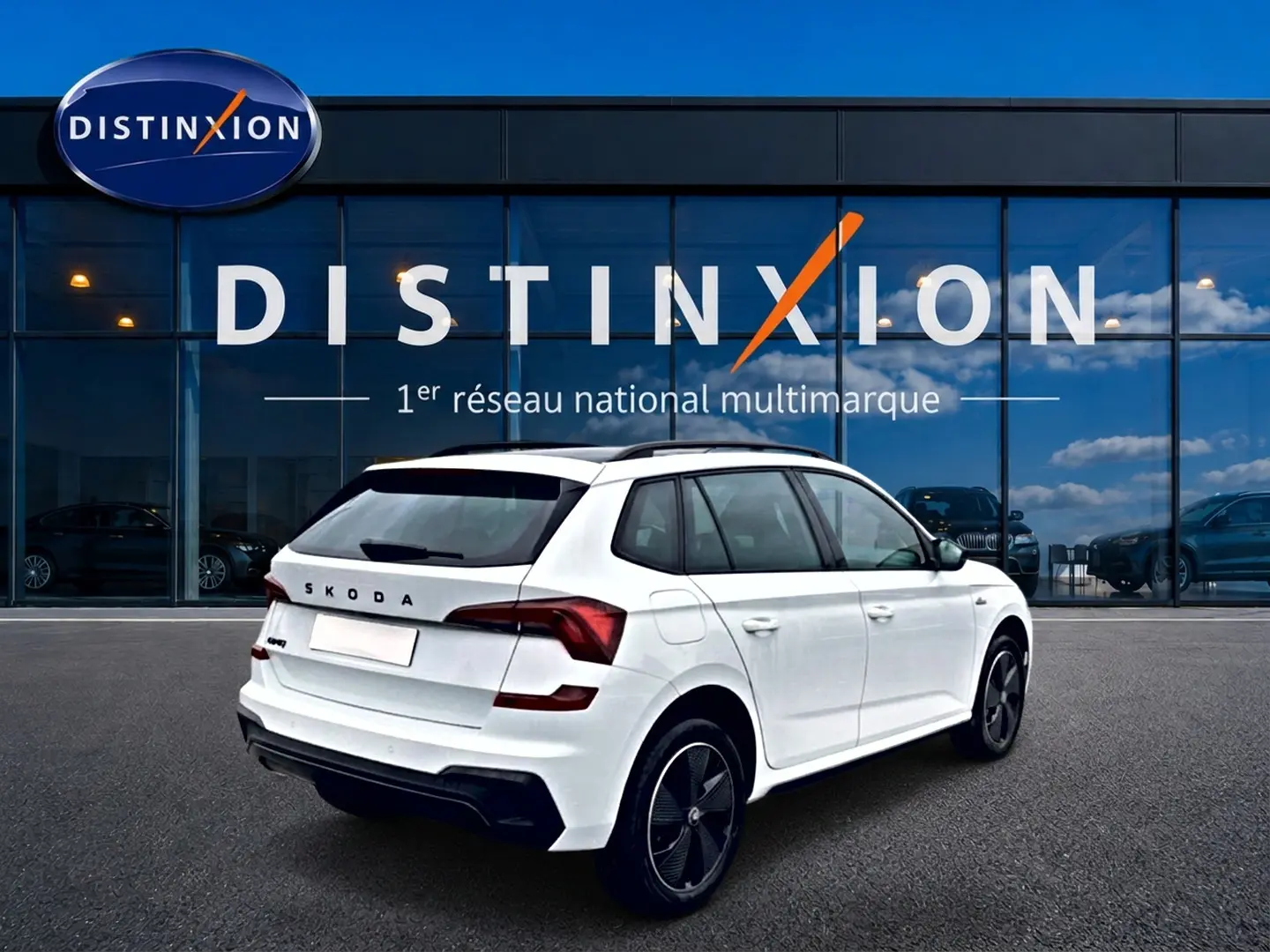 Vue 3/4 arrière droite d'un Skoda Kamiq blanc nacré avec jantes noires et toit panoramique, devant un showroom Distinxion.