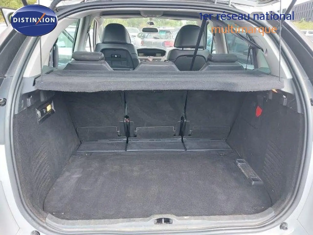 Coffre ouvert d'une Citroën C4 Picasso gris alu métal, vue arrière montrant l'espace de chargement et les sièges rabattus.