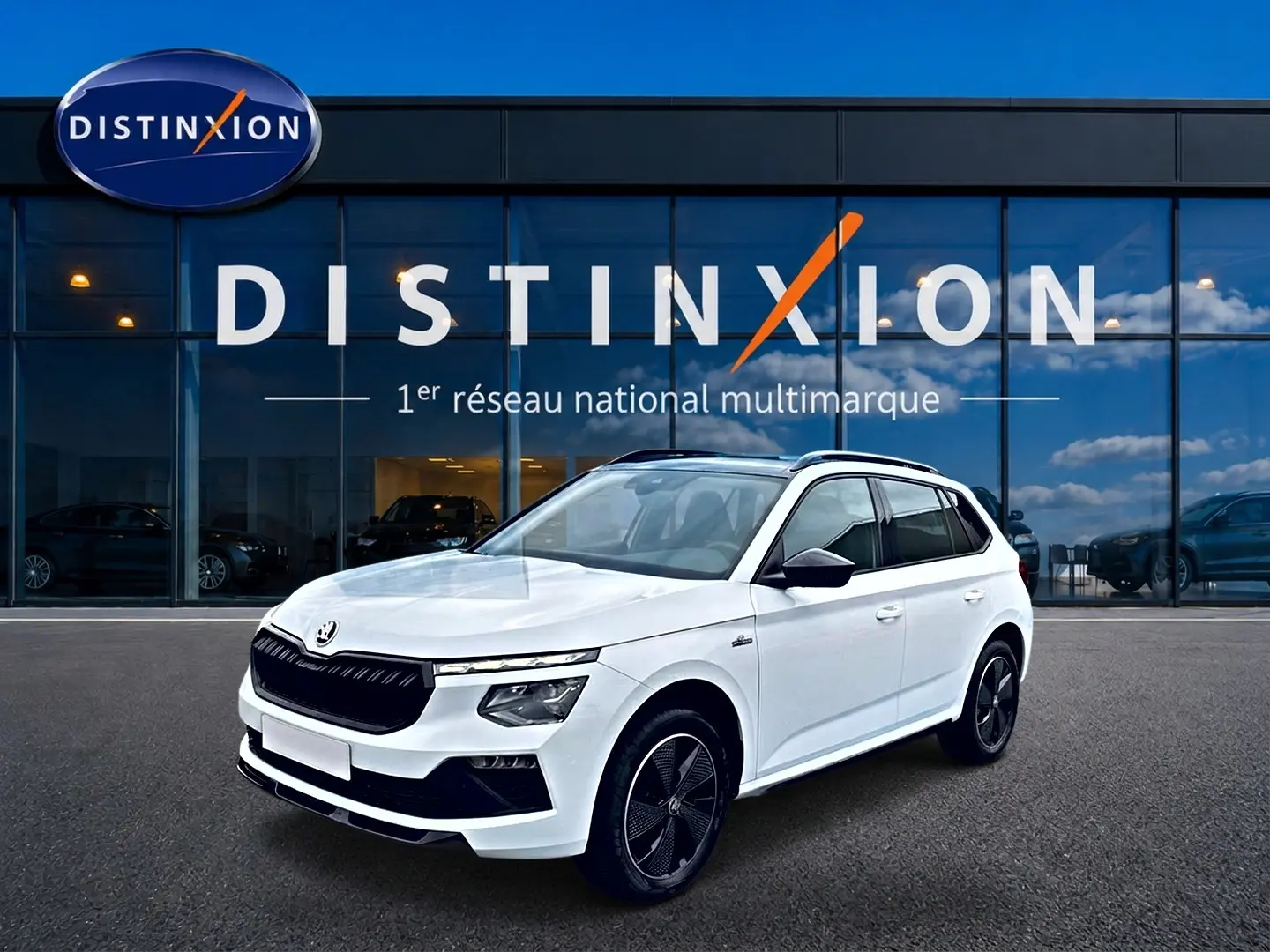 Vue 3/4 avant droite d'un Skoda Kamiq blanc nacré avec jantes noires et toit panoramique devant un showroom Distinxion.