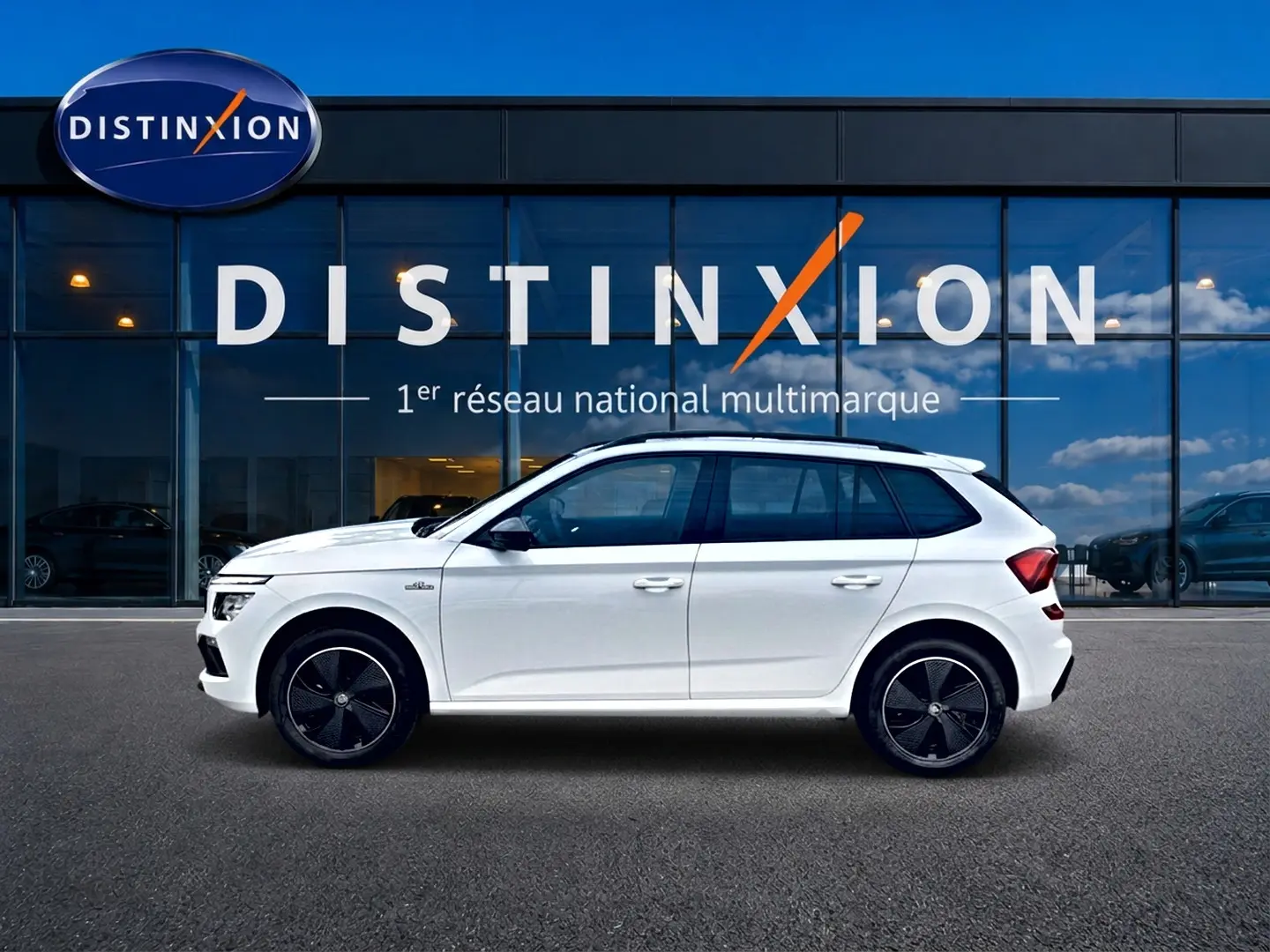 Profil droit d'un Skoda Kamiq blanc nacré 2026 avec jantes noires et toit panoramique visible, devant une vitrine Distinxion.