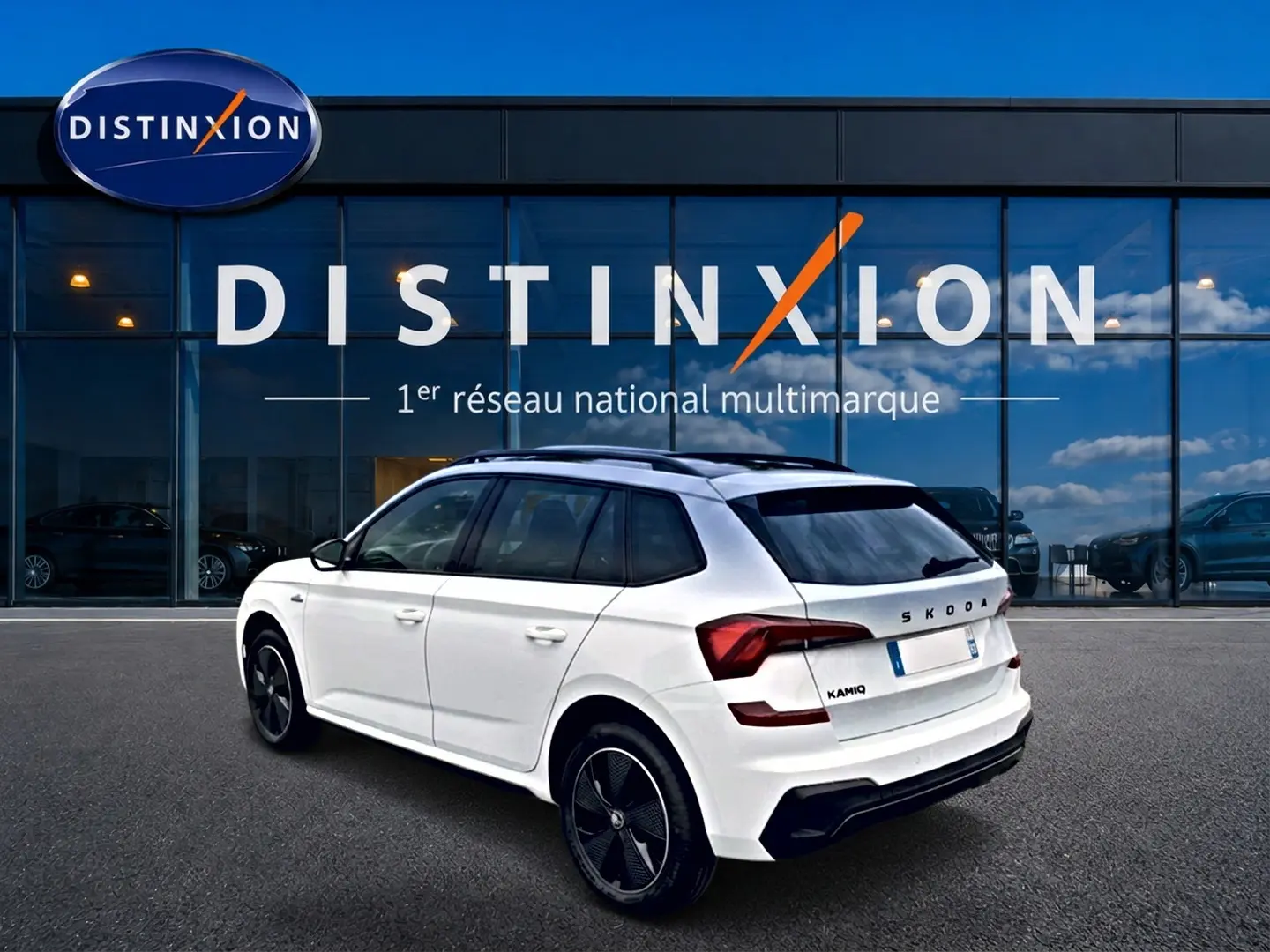 Vue 3/4 arrière droite d'un Skoda Kamiq blanc nacré avec jantes noires et toit panoramique, devant une vitrine Distinxion.