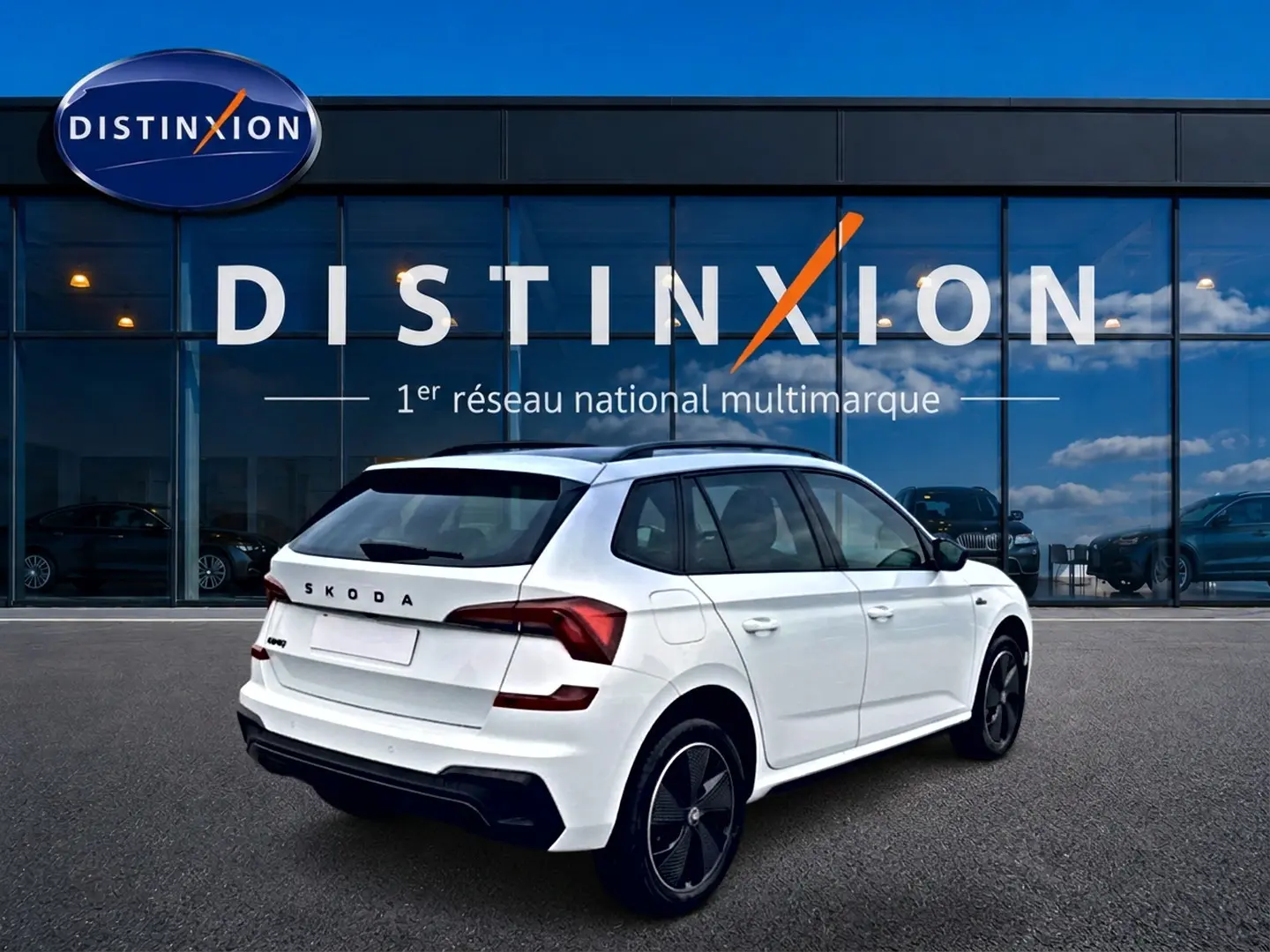 Vue 3/4 arrière droite d’un Skoda Kamiq blanc nacré avec jantes noires et toit panoramique, devant une vitrine Distinxion.