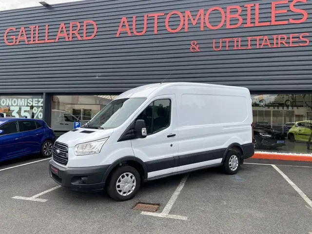 Fourgon Ford Transit blanc vu en 3/4 avant droit, stationné devant un garage avec marquage noir sur bas de caisse.
