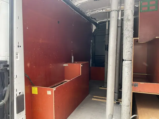 Intérieur du Ford Transit Fourgon blanc vu de la porte latérale, montrant l'aménagement en bois et les cloisons internes.