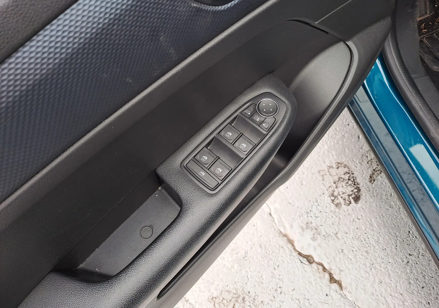 Gros plan sur la commande des vitres électriques côté gauche de la porte d'une Renault Arkana bleu Zanzibar 2023.