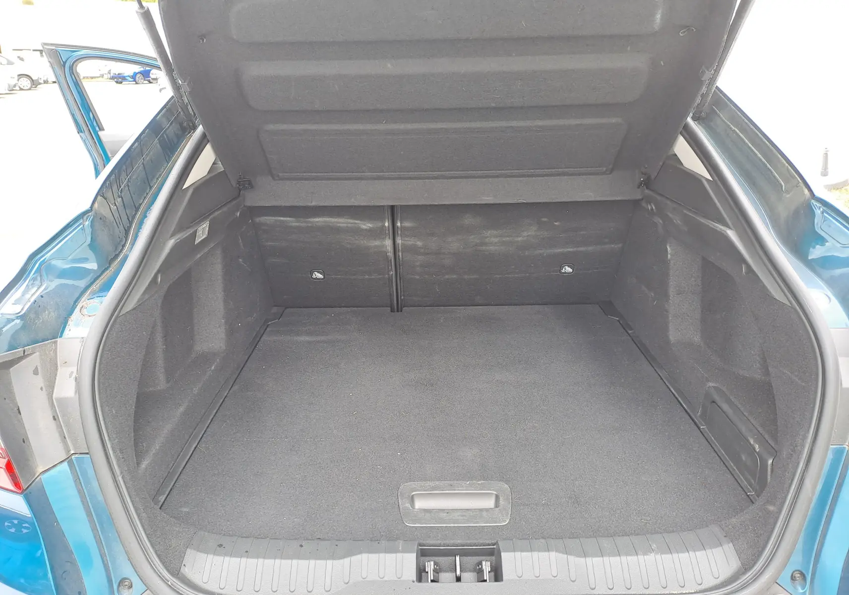 Coffre ouvert vu de l'arrière d'une Renault Arkana bleu Zanzibar metal, montrant l'espace de rangement vide.