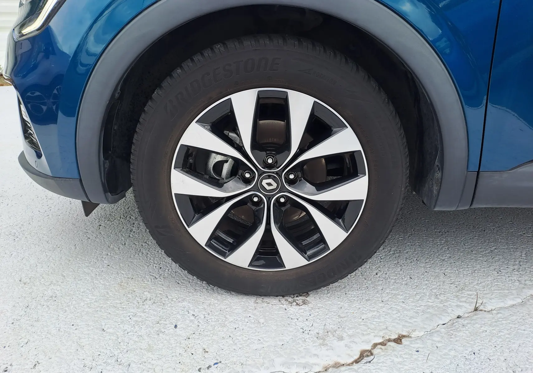 Gros plan sur la roue avant gauche du Renault Arkana bleu Zanzibar métal avec jante alliage bicolore et logo central Renault.