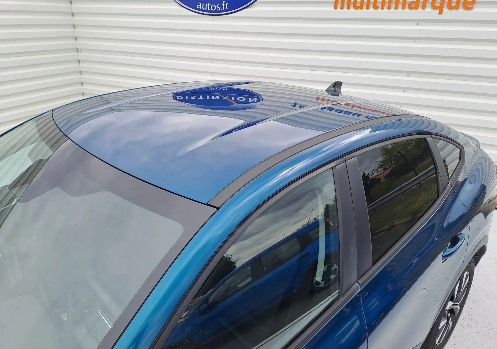 Vue plongeante côté gauche sur Renault Arkana 2023 bleu Zanzibar métallisé avec toit panoramique et vitres teintées.
