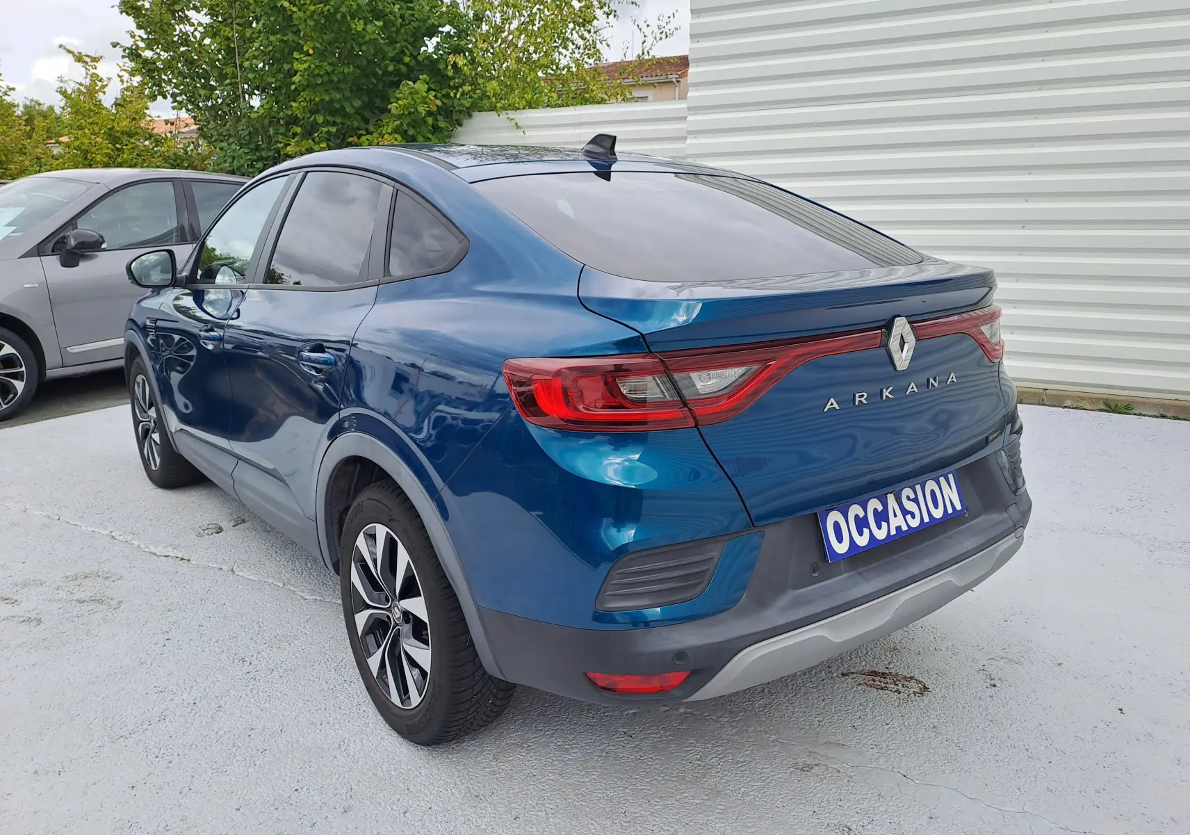 Vue 3/4 arrière droite d'une Renault Arkana bleu Zanzibar métal avec feux arrière allongés et plaque "OCCASION" visible.