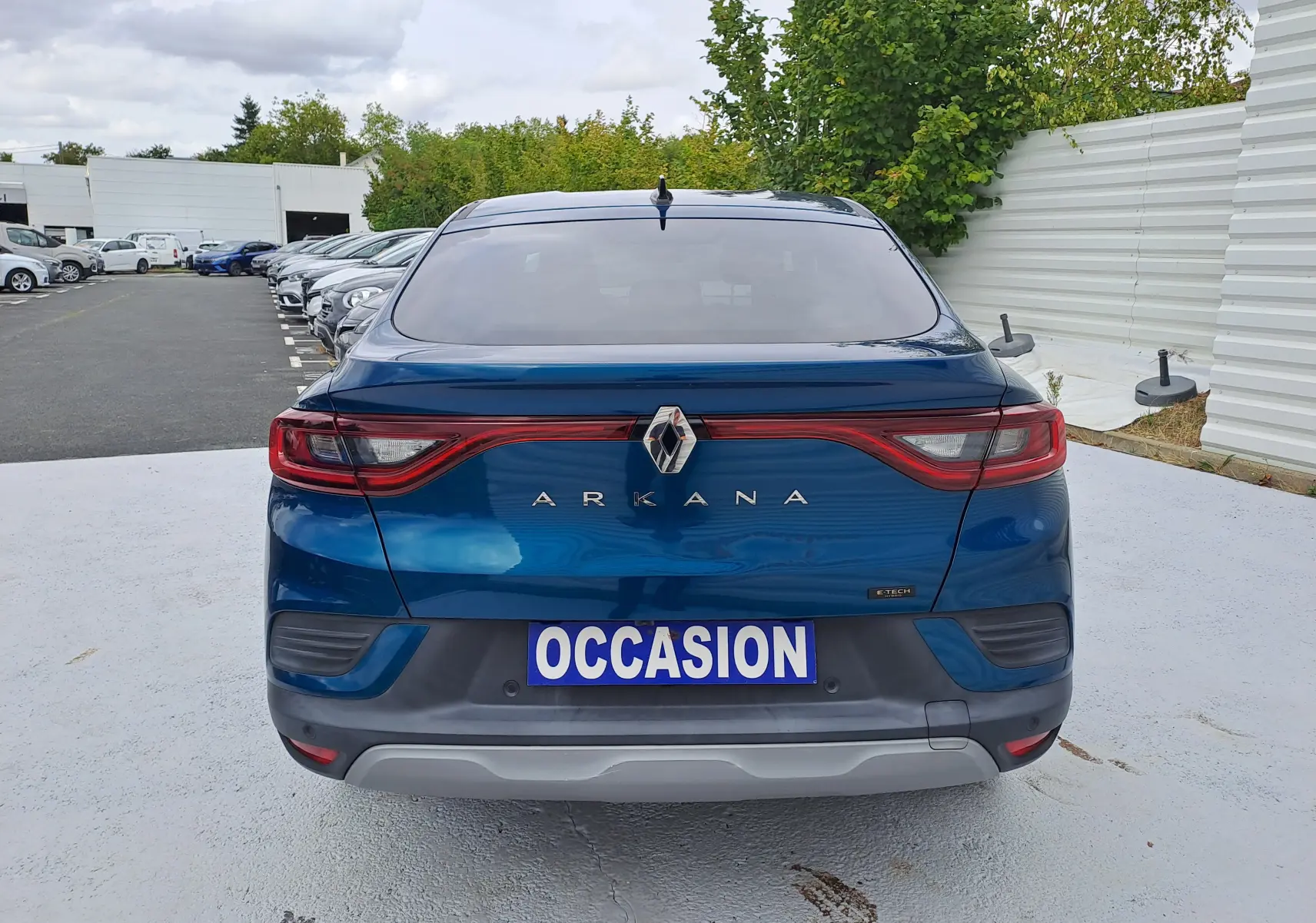 Vue arrière d'un Renault Arkana bleu Zanzibar métallisé avec feux arrière reliés et plaque "OCCASION" visible.