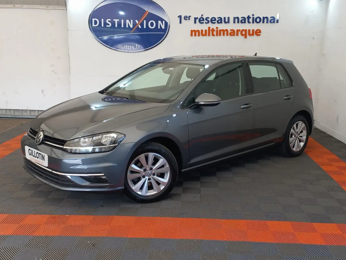 Volkswagen Golf gris foncé vue 3/4 avant droit en intérieur, avec jantes alliage et calandre chromée.