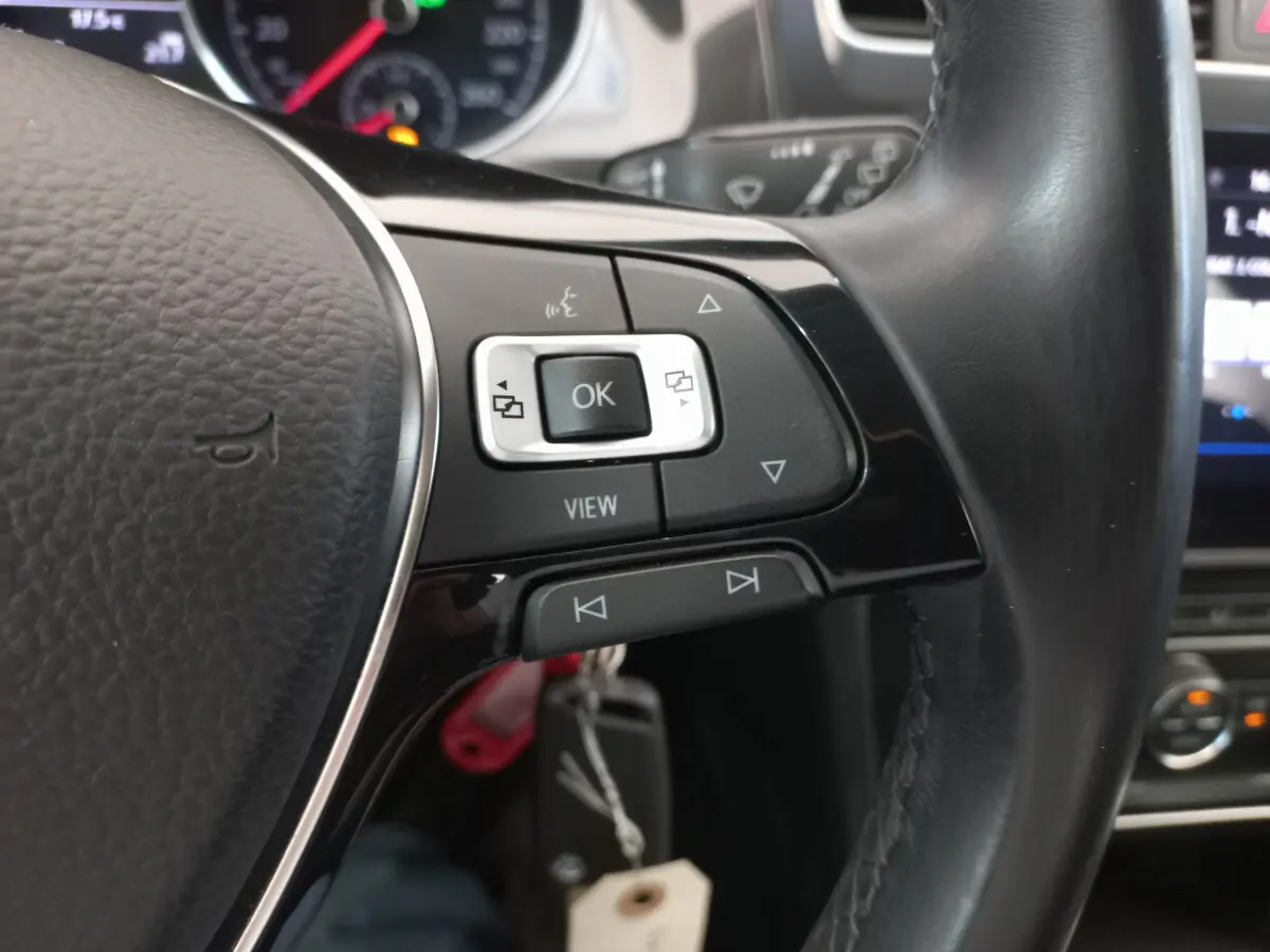 Gros plan sur les commandes gauche du volant cuir noir d'une Volkswagen Golf gris foncé, avec tableau de bord en arrière-plan.