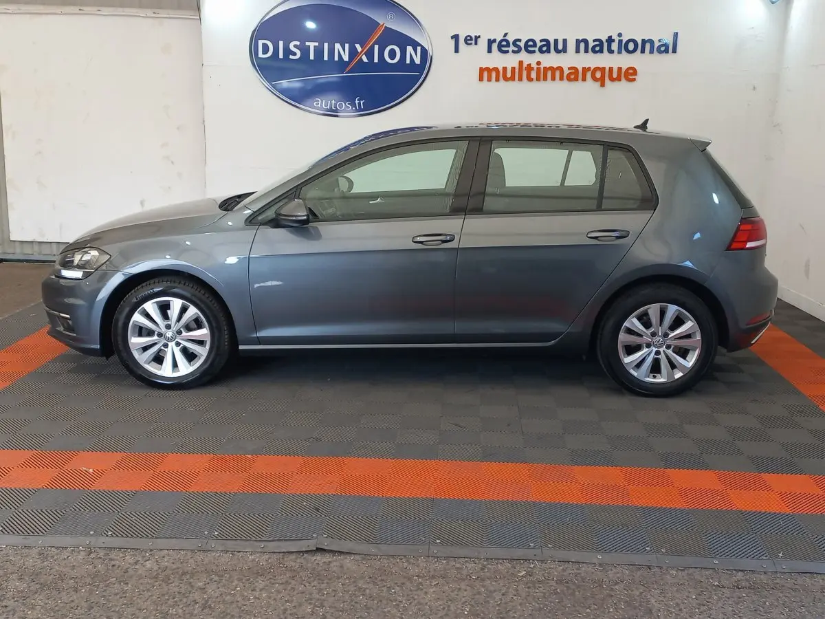 Profil droit d'une Volkswagen Golf gris foncé 2019 garée en intérieur sur sol à damier gris et orange.