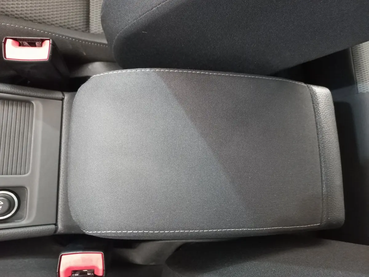 Accoudoir central en tissu gris foncé dans l'habitacle d'une Volkswagen Golf 2019, avec ceintures de sécurité rouges visibles.