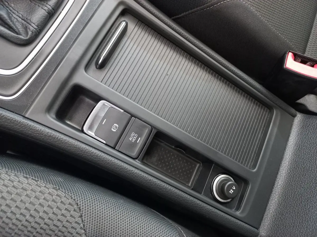 Gros plan sur la console centrale noire de la Volkswagen Golf 1.0 TSI 2019 avec frein à main électrique et prise 12V.