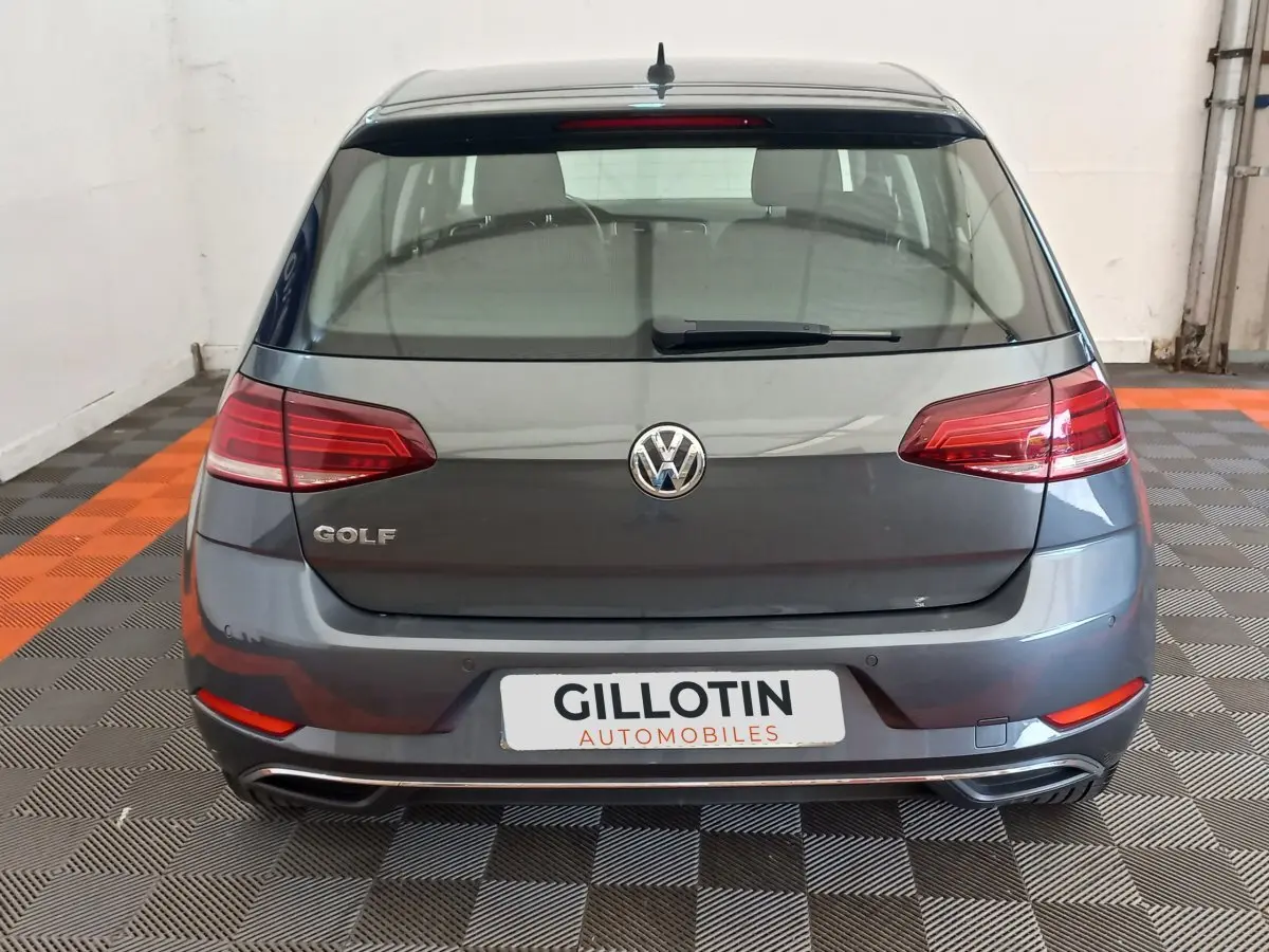 Vue arrière d'une Volkswagen Golf gris foncé stationnée sur un sol à damiers noir et orange, avec feux arrière LED.