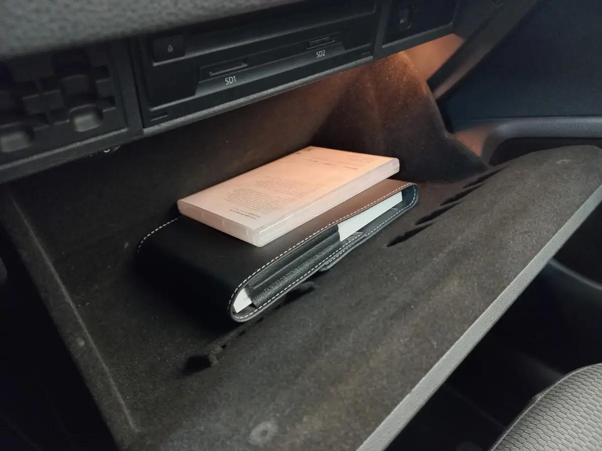 Vue rapprochée de la boîte à gants ouverte d'une Volkswagen Golf gris foncé, avec un manuel et une pochette noire à l'intérieur.