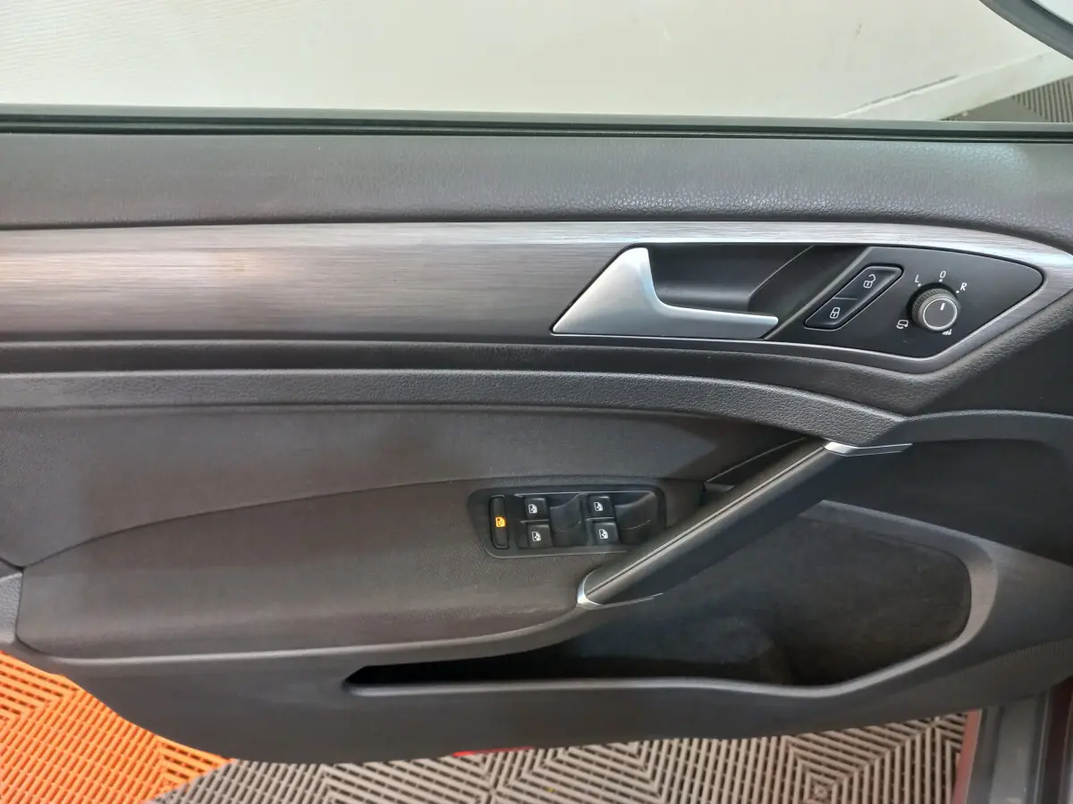 Vue rapprochée de la porte côté gauche de la Volkswagen Golf gris foncé avec commandes électriques et poignée argentée.