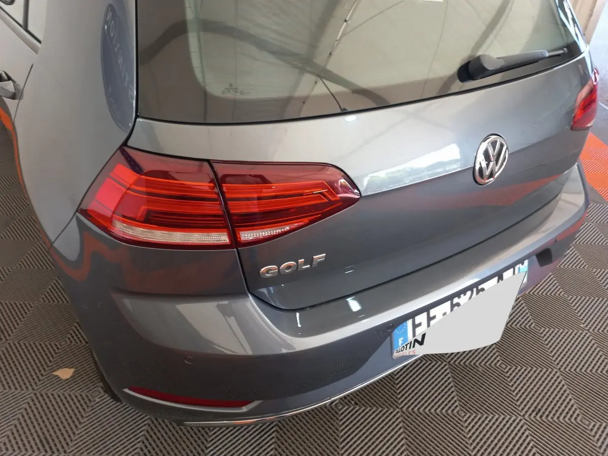 Vue arrière en 3/4 gauche d'une Volkswagen Golf gris foncé avec feux arrière LED et logo distinctif sur le coffre.