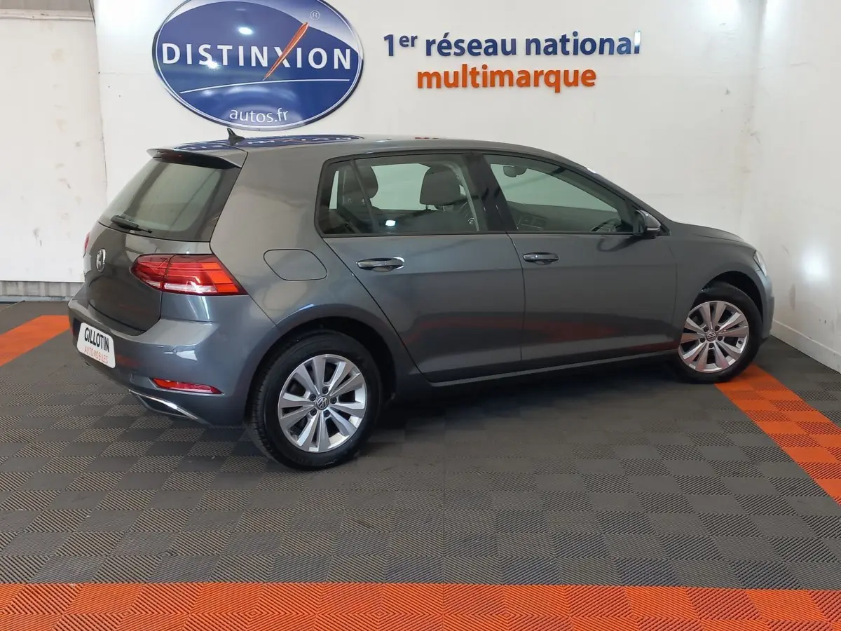 Volkswagen Golf gris foncé vue de profil côté droit dans un showroom avec logo Distinxion en arrière-plan