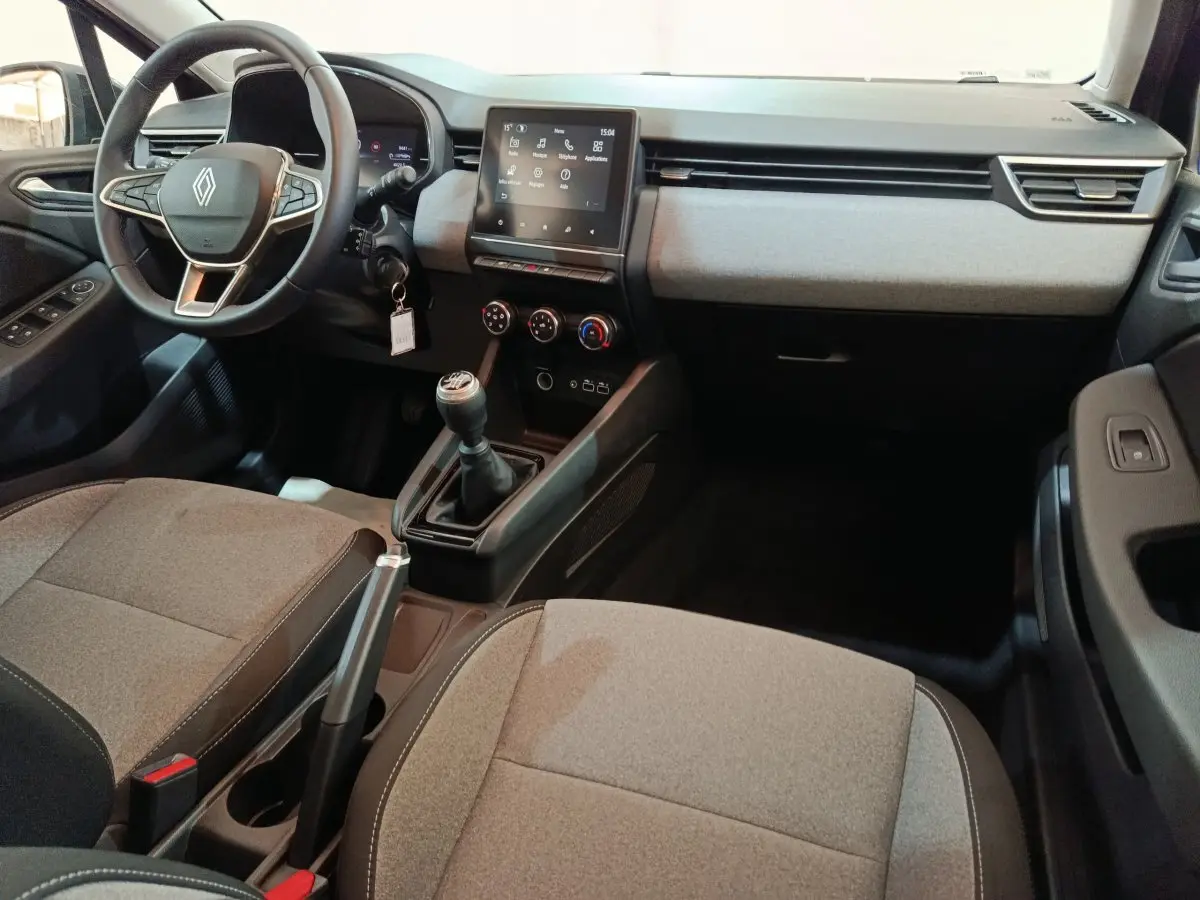 Intérieur gris clair de Renault Clio 2025, vue du tableau de bord avec volant, écran tactile et boîte manuelle.