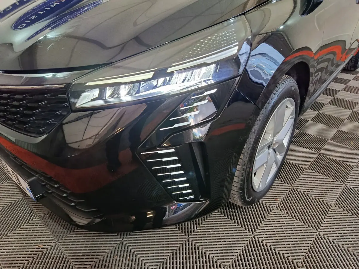 Vue 3/4 avant droit d'une Renault Clio noire 2025 avec phares LED et jantes alliage visibles sur sol damier.