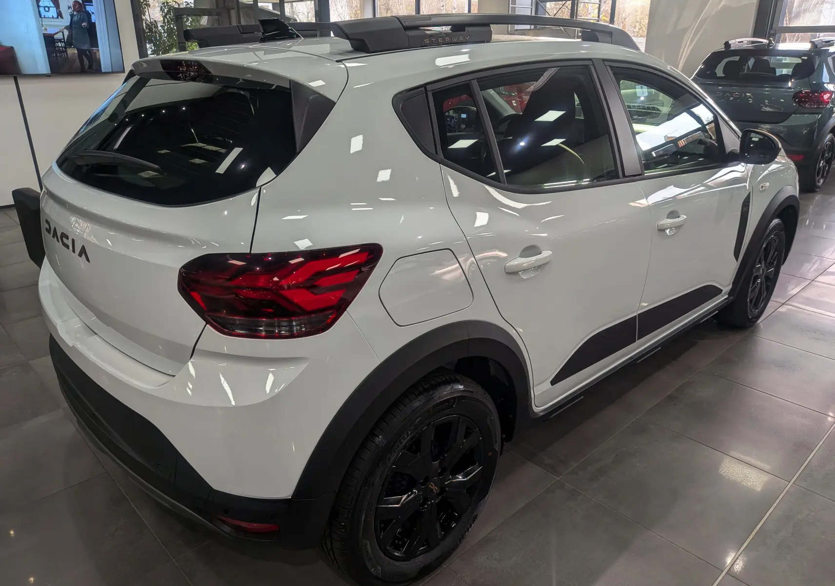 Vue latérale droite d'une Dacia Sandero Stepway TCe 110 Blanc Glacier avec jantes noires en showroom.