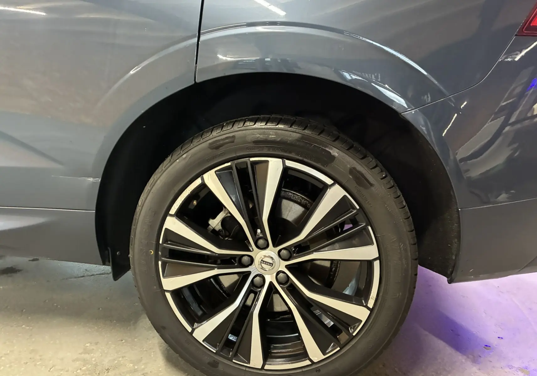 Gros plan sur la roue arrière droite d’un Volvo XC60 bleu 2023 avec jante alliage 20'' noir et diamant.