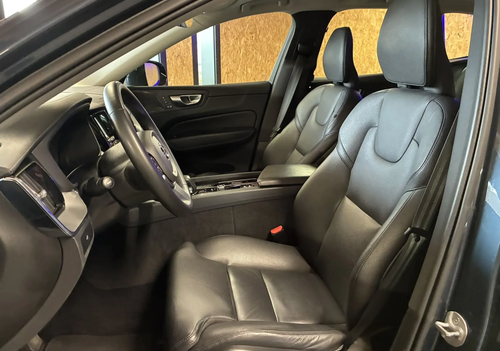 Vue intérieure côté conducteur du Volvo XC60 2023, sièges en cuir noir avec planche de bord et volant multifonctions.