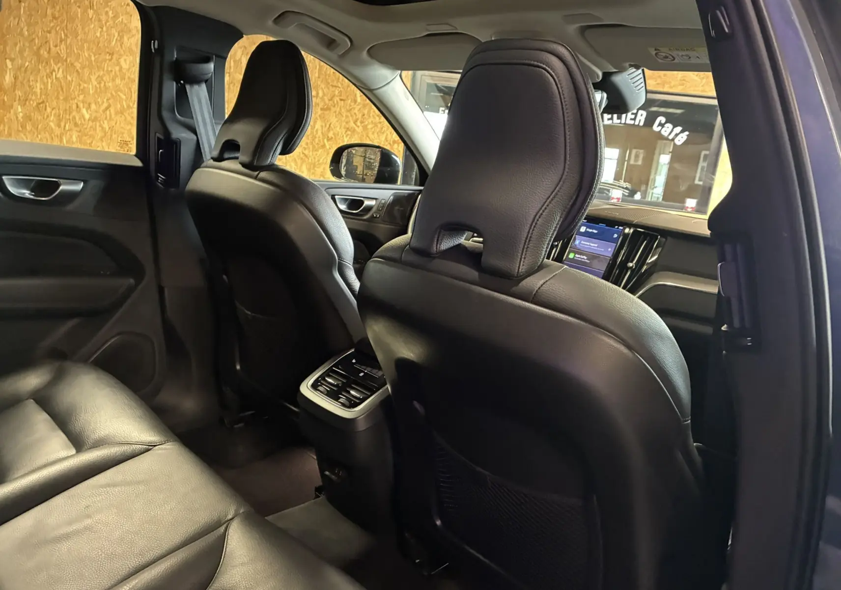 Vue intérieure arrière du Volvo XC60 bleu 2023, sièges cuir noirs et console centrale avec commandes climatisation.