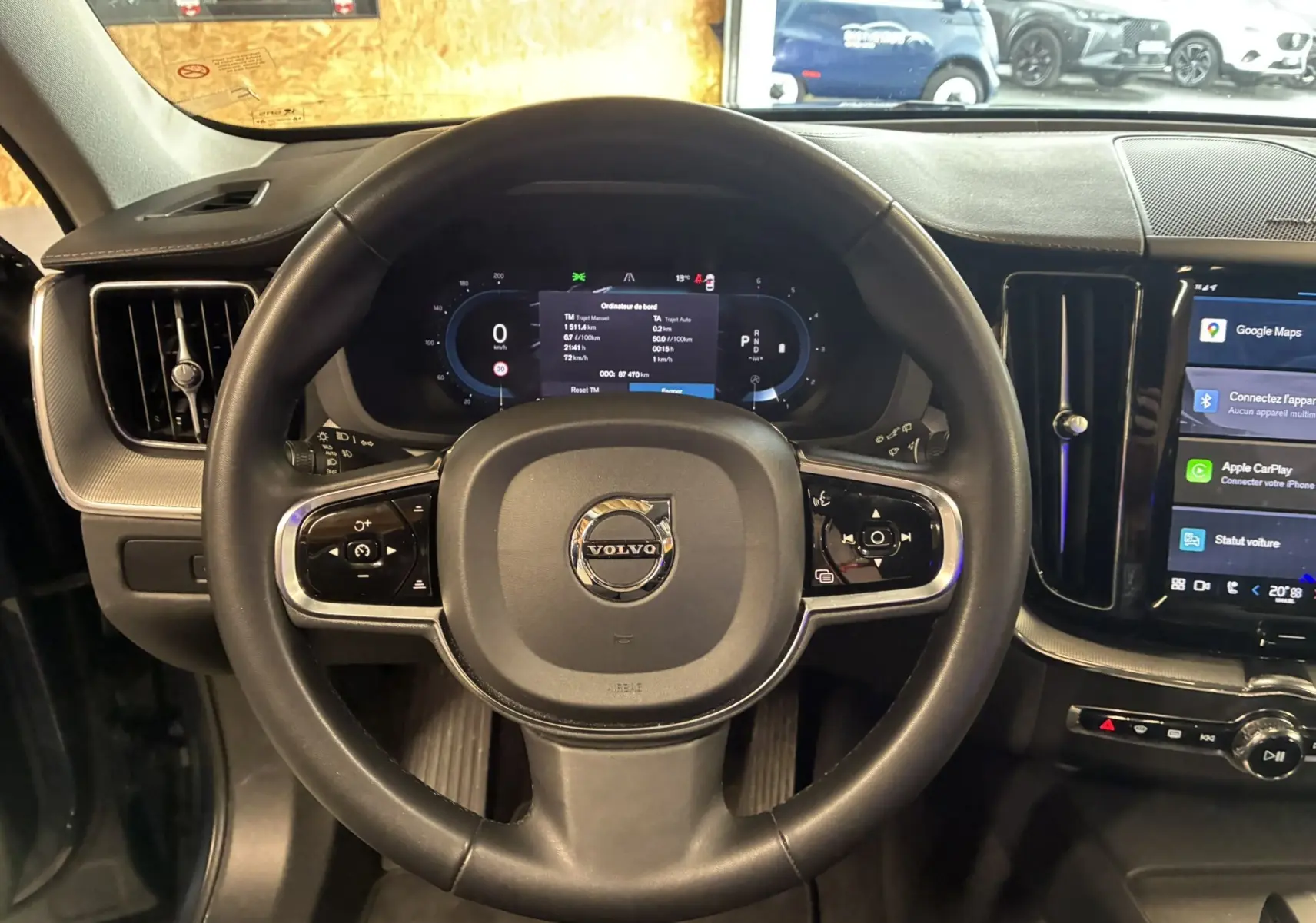 Vue intérieure centrée sur le volant noir du Volvo XC60 2023 avec tableau de bord numérique et écran tactile latéral.